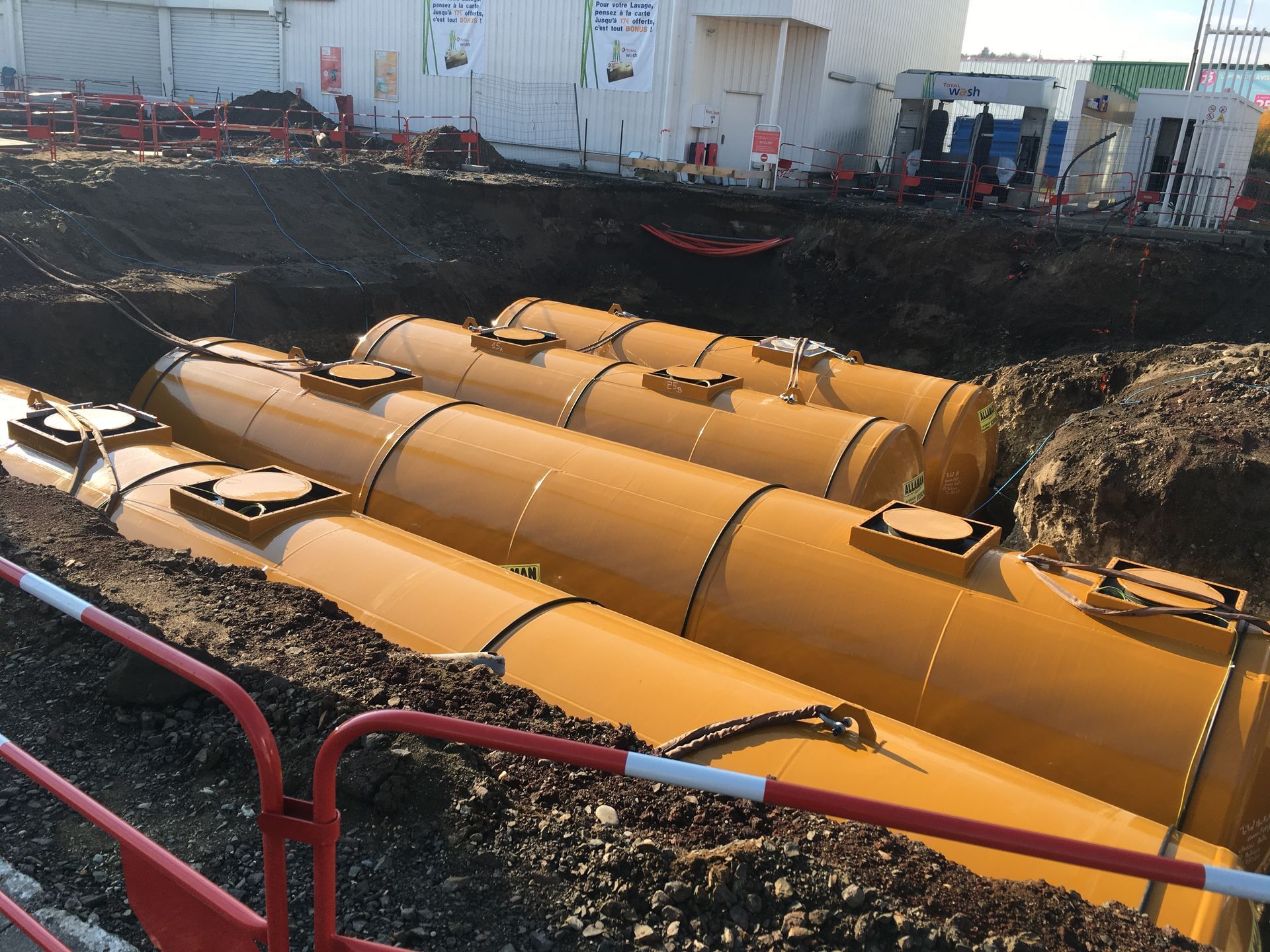 Réservoirs cylindriques jaunes enfouis dans la terre, à côté d'un chantier de construction.