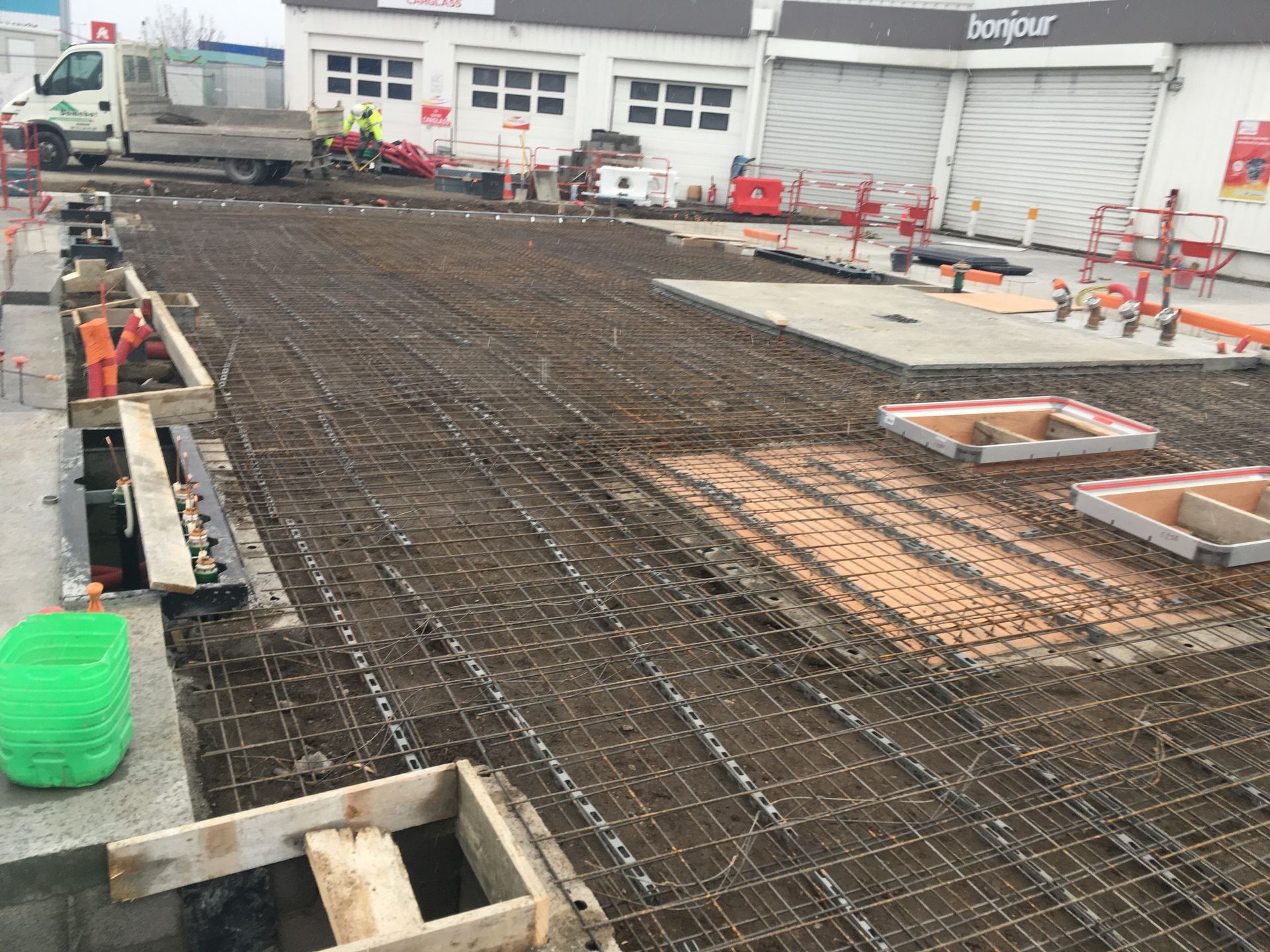 Chantier de construction montrant un terrain en terre battue préparé avec un treillis métallique et des coffrages