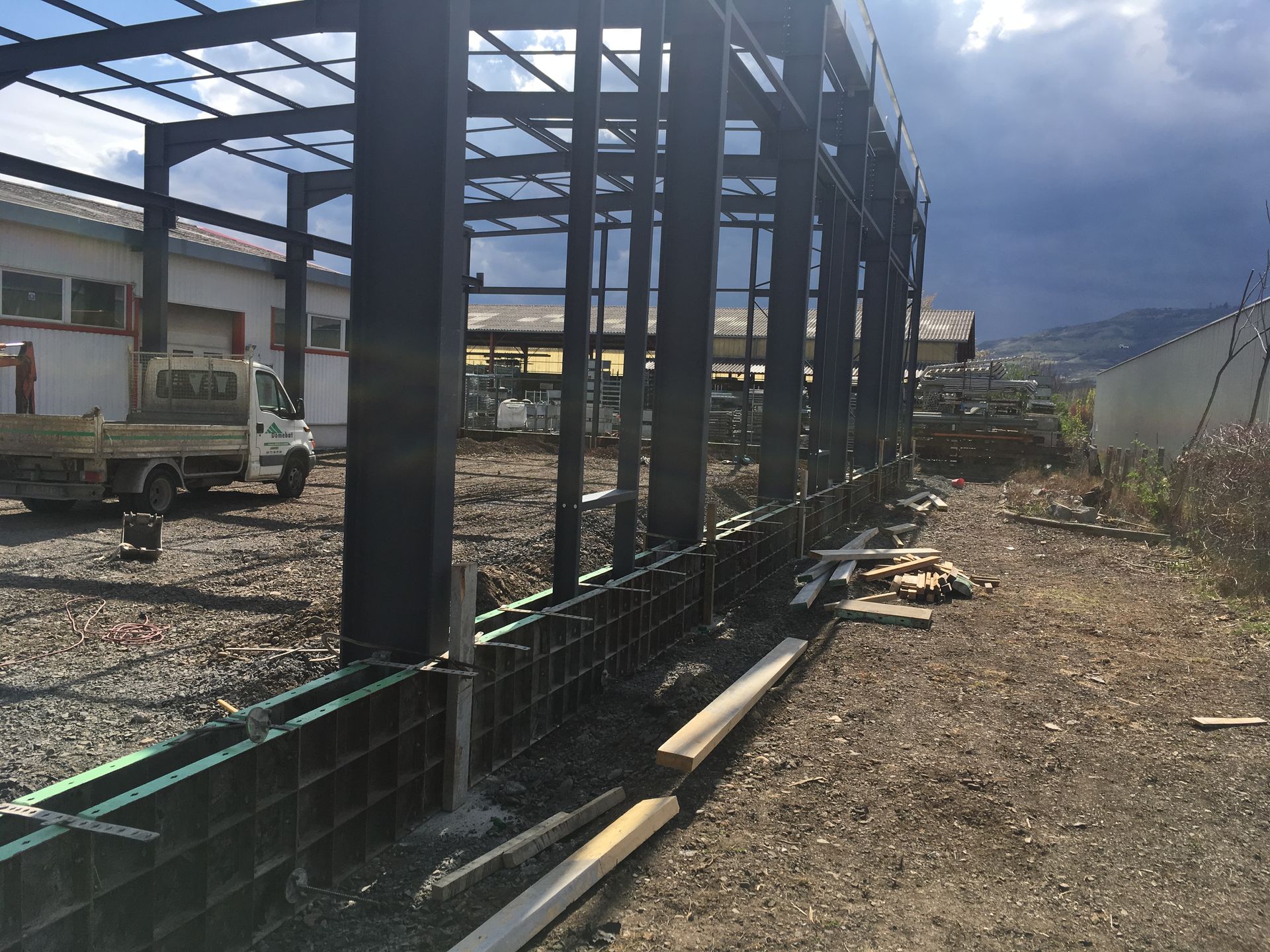 Chantier : bâtiment à ossature métallique en construction, coffrage vert foncé, ciel couvert.