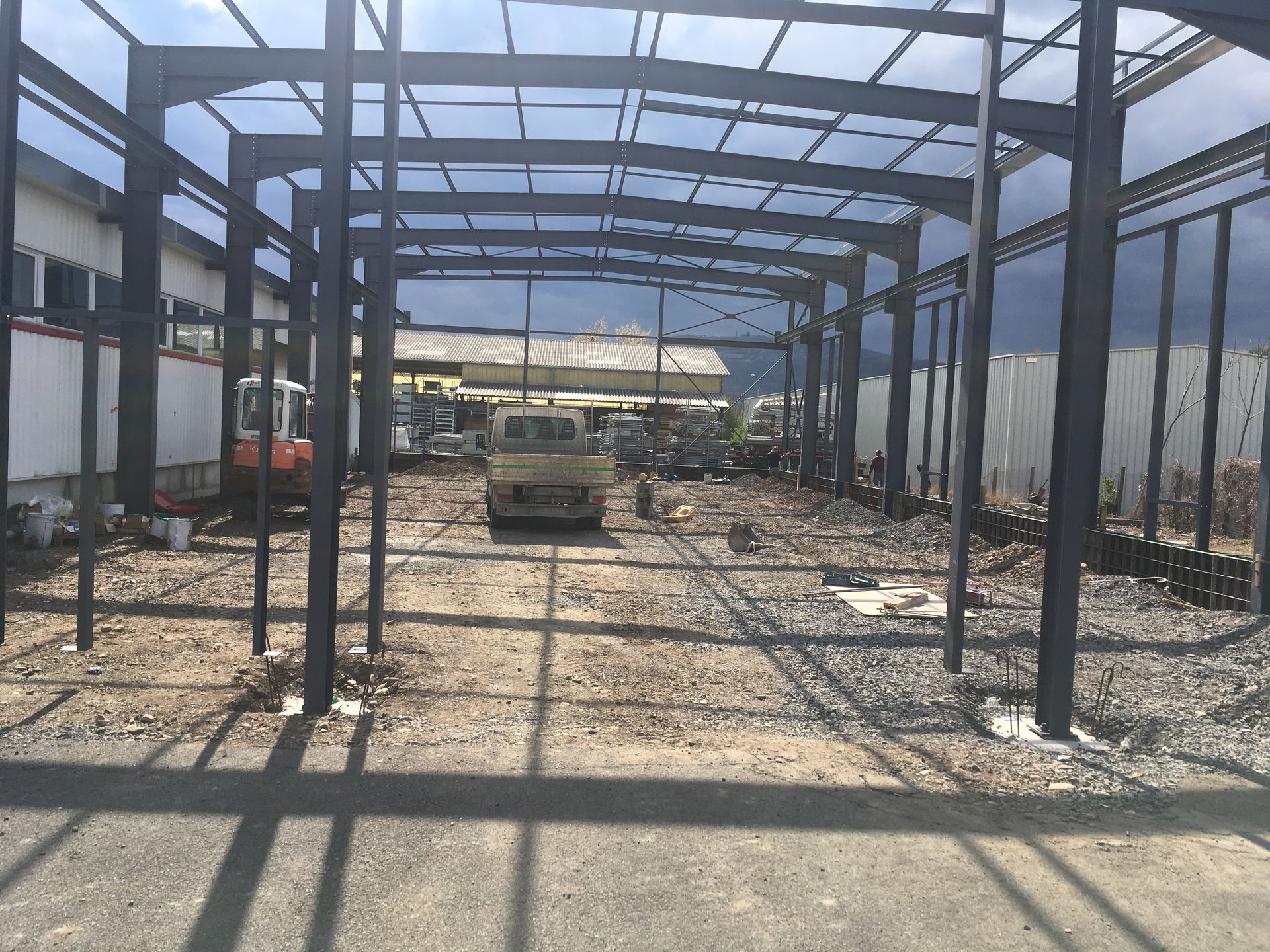 Une structure à ossature métallique en construction sur un terrain vague, avec un véhicule et des engins de chantier