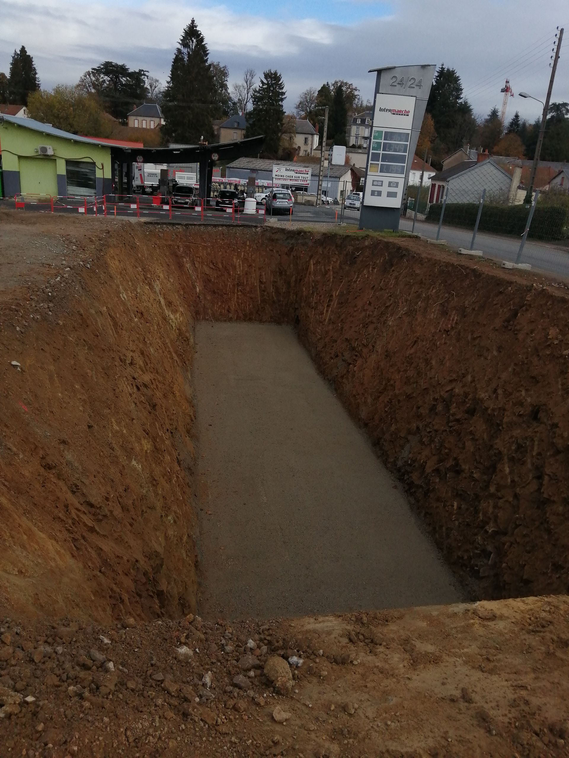 Une excavation rectangulaire remplie de gravier, jouxtant une rue.