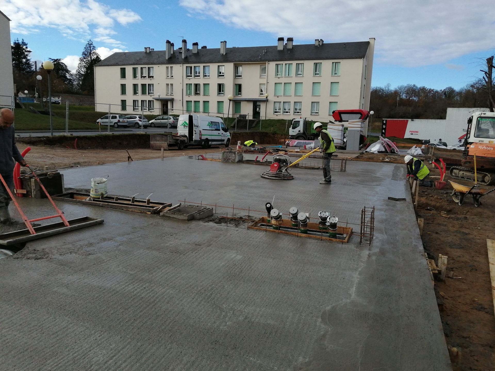 Des ouvriers du bâtiment lissent du béton frais, avec des bâtiments en arrière-plan.