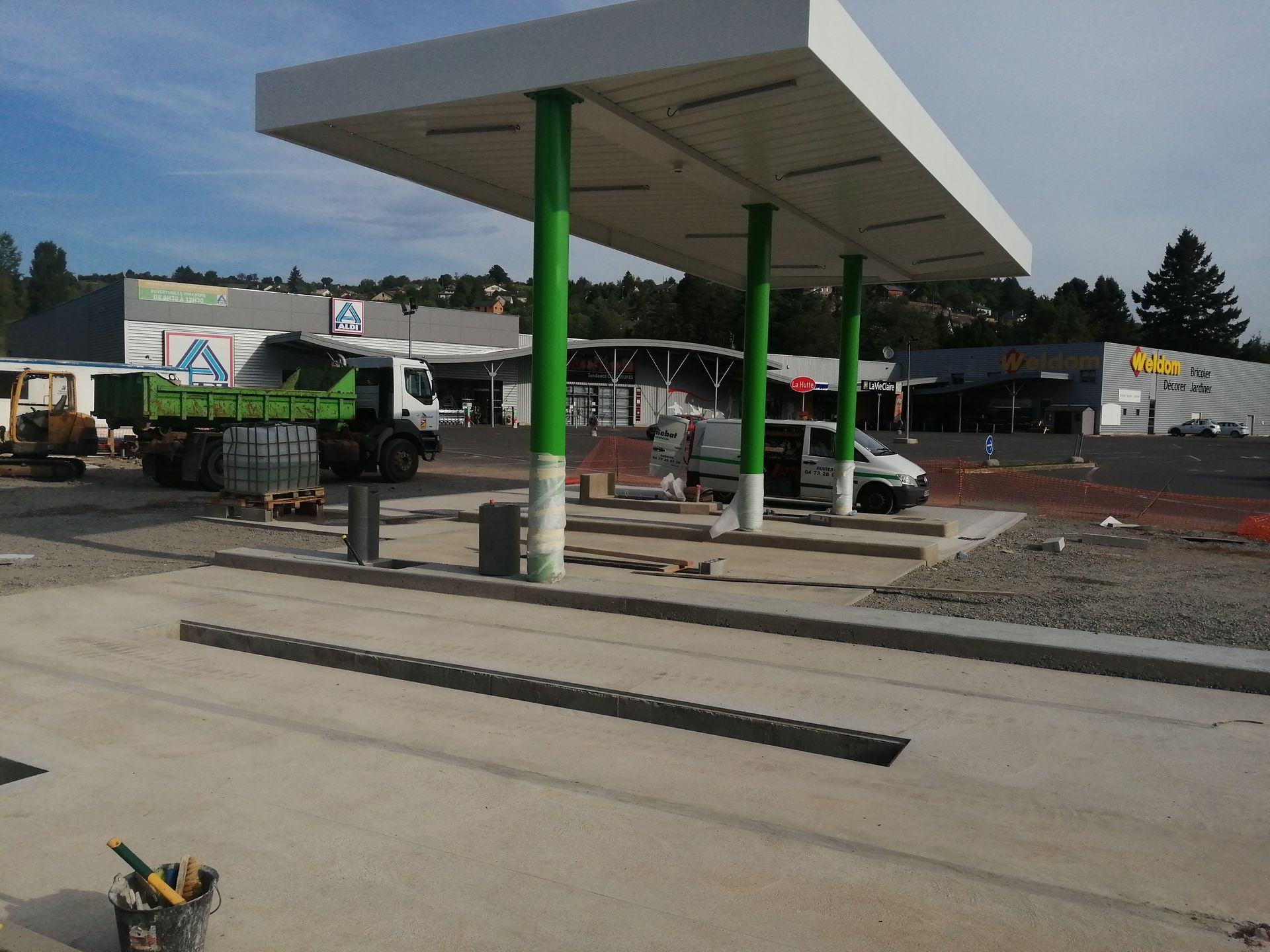 Une station-service en construction, avec des supports verts, un toit blanc et un camion garé à côté.