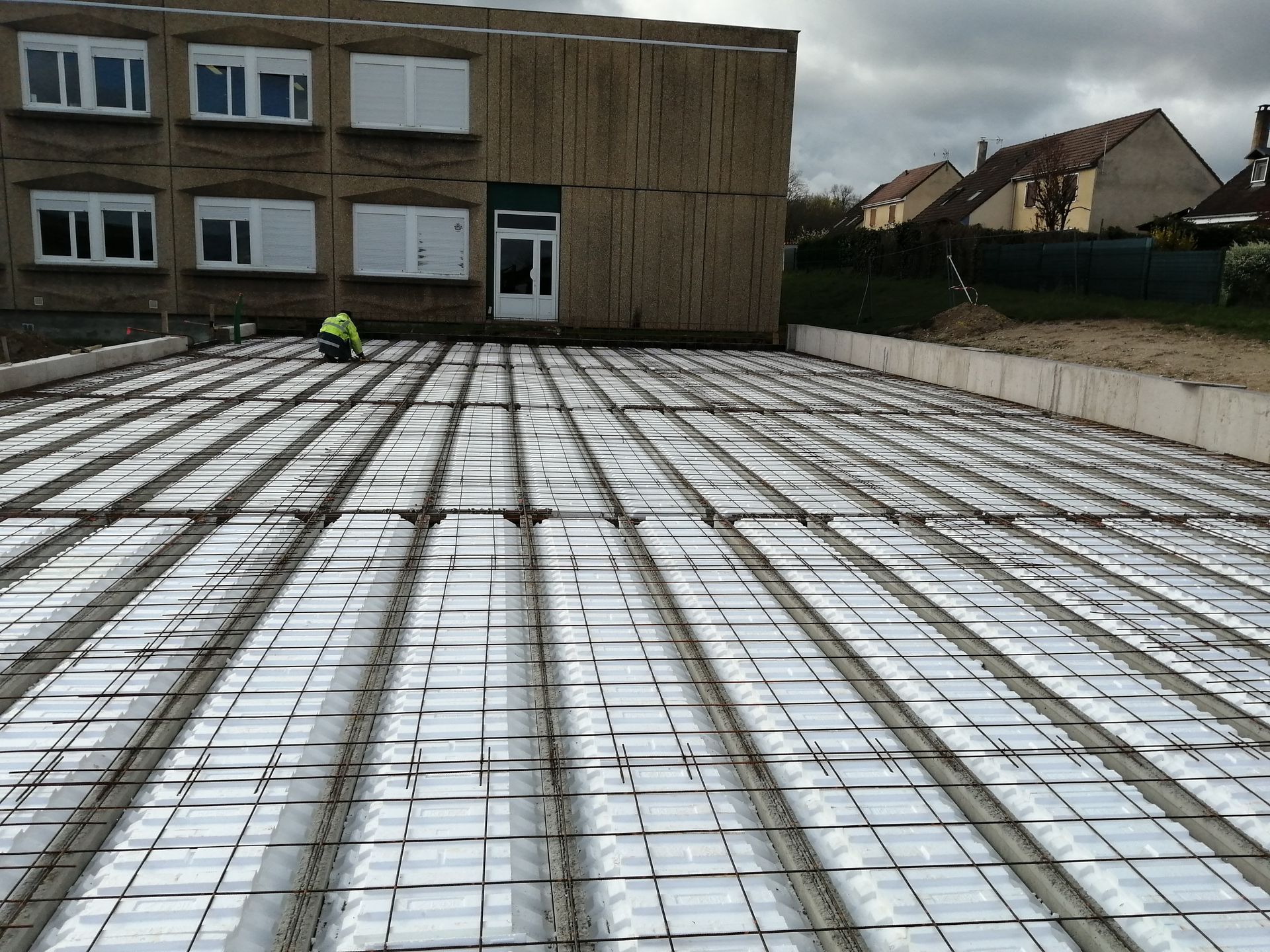 Un ouvrier du bâtiment agenouillé sur une structure de plancher composée de blocs d'isolation thermique blancs