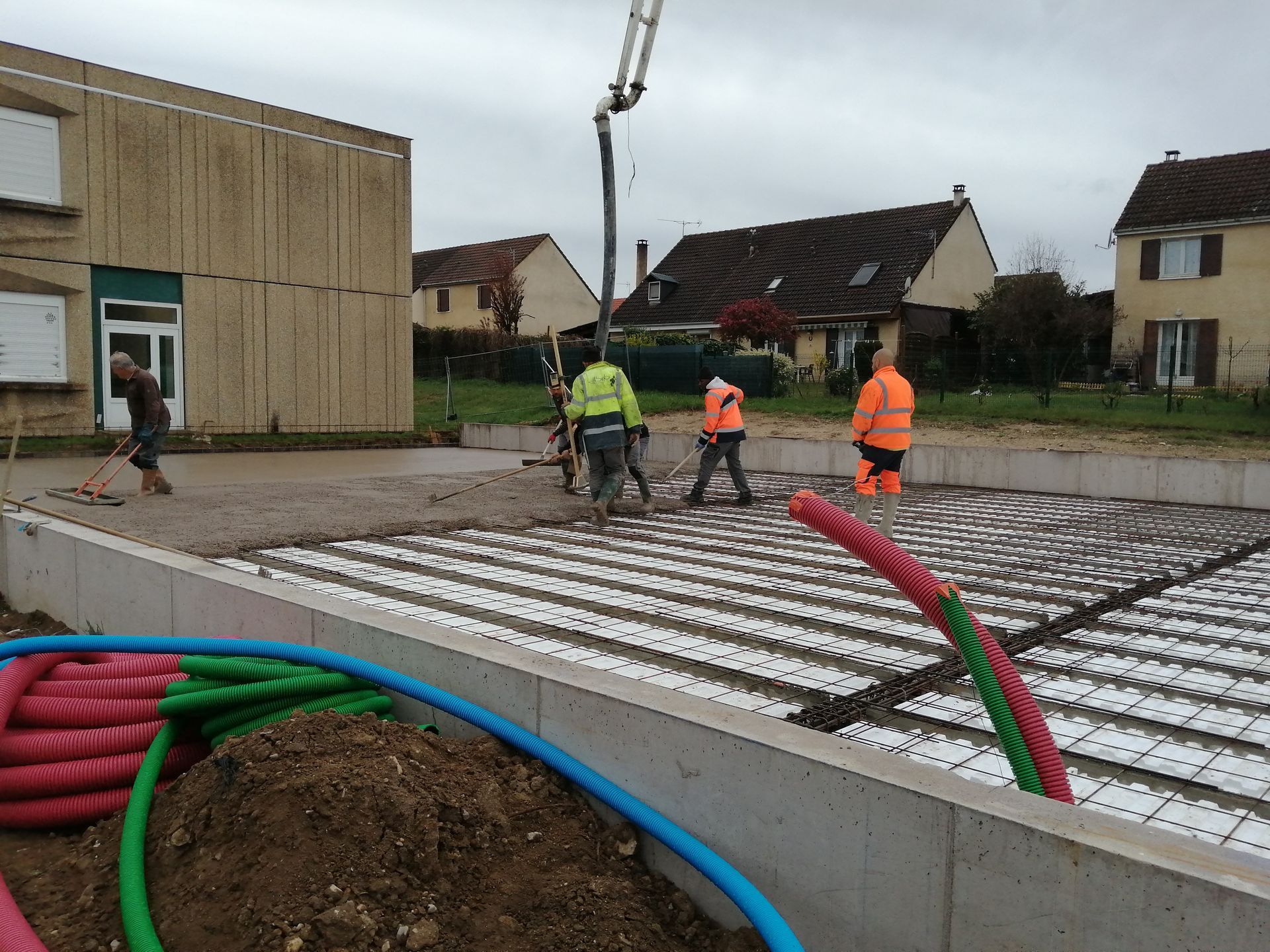 Des ouvriers du bâtiment coulent du béton sur des panneaux d'isolation blancs sur un chantier de construction résidentielle.