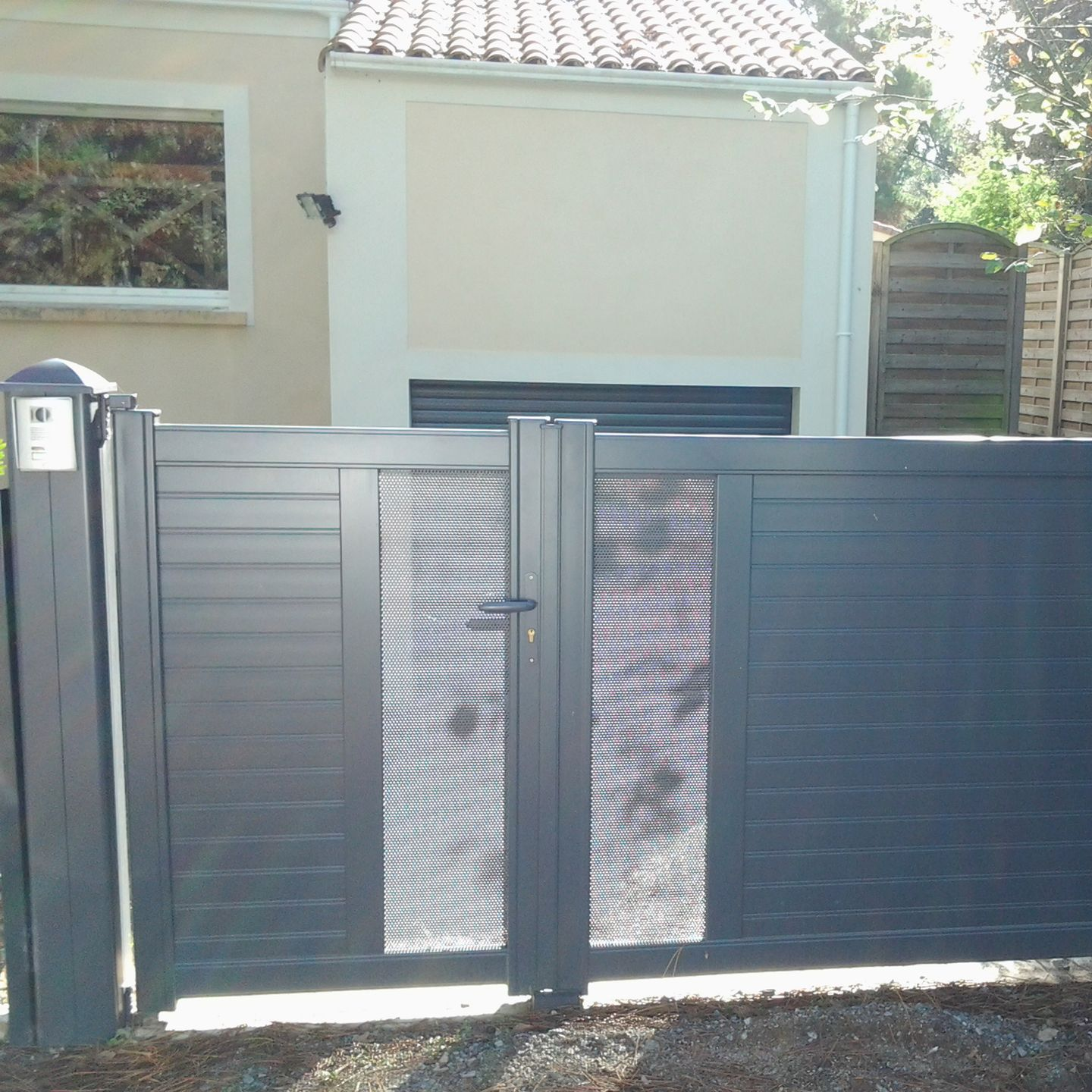 Portail en métal noir avec panneaux centraux en treillis devant un bâtiment beige clair.