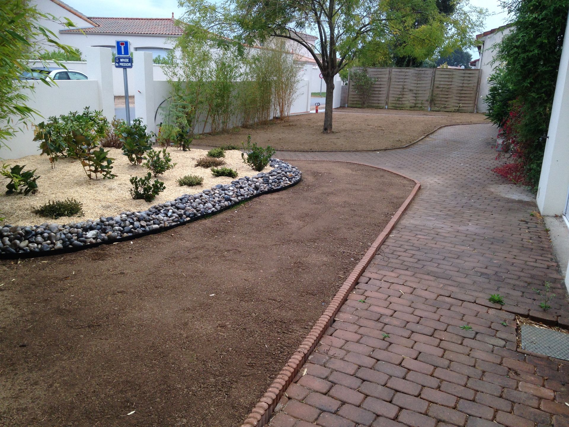 Une cour recouverte de gravier avec un chemin de briques et un petit jardin bordé de rochers sombres.