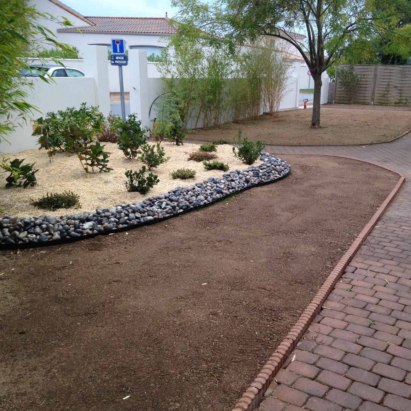 Un jardin paysager avec une bordure de pierres, des arbustes et une allée de briques.