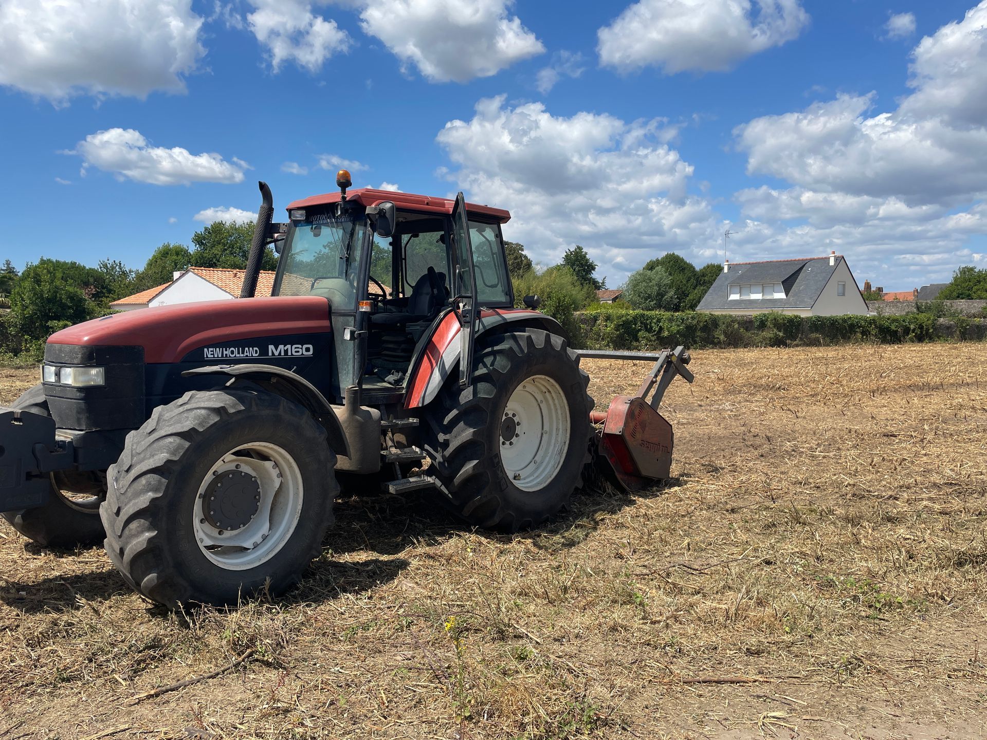 Un tracteur rouge laboure un champ sous un ciel bleu.