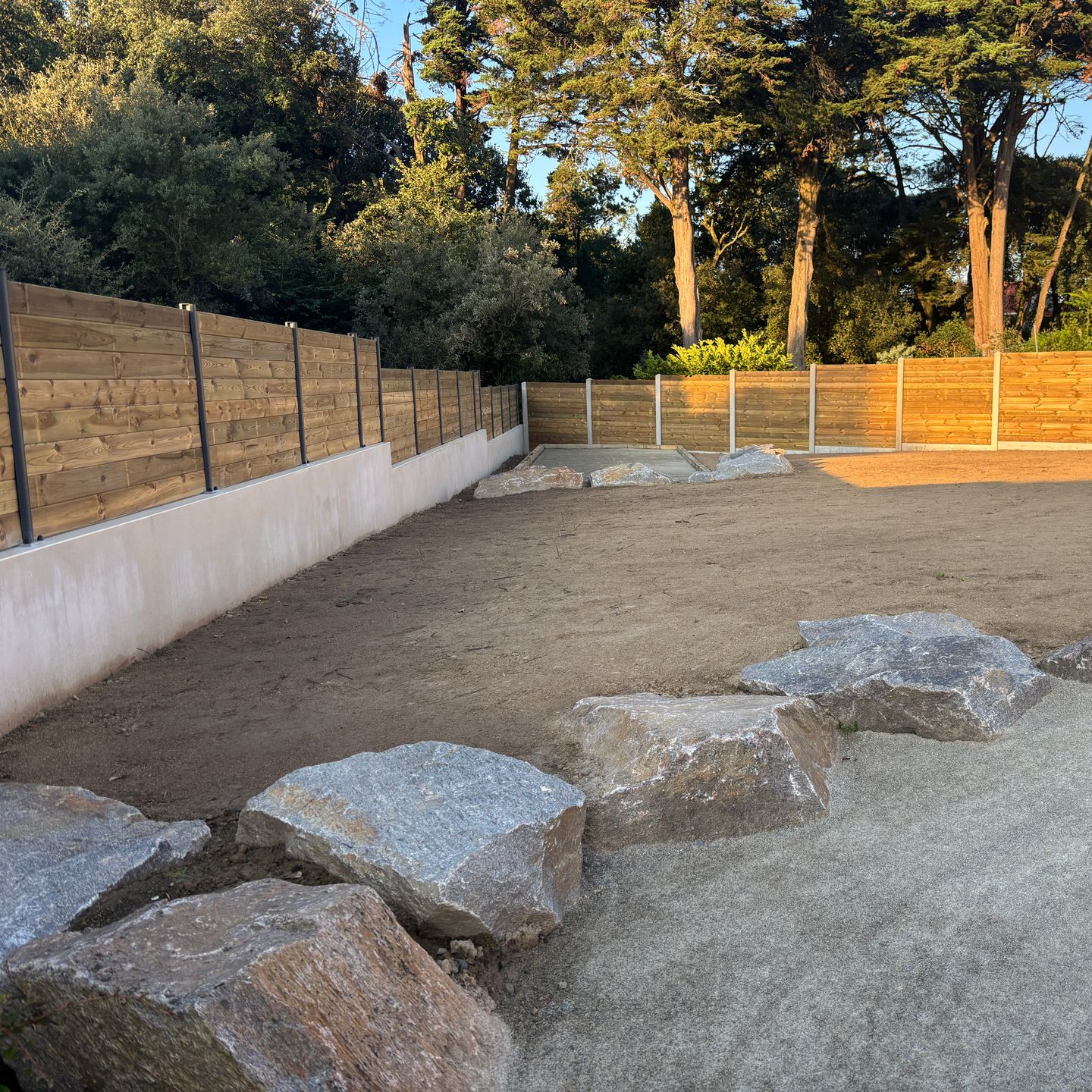 Une cour arrière avec un lit de gravier, de gros rochers et une clôture en bois.