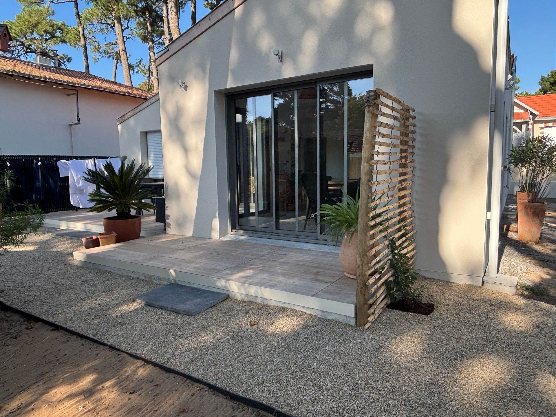 Extérieur de maison moderne avec portes coulissantes en verre, moustiquaire en bois et aménagement paysager en gravier.