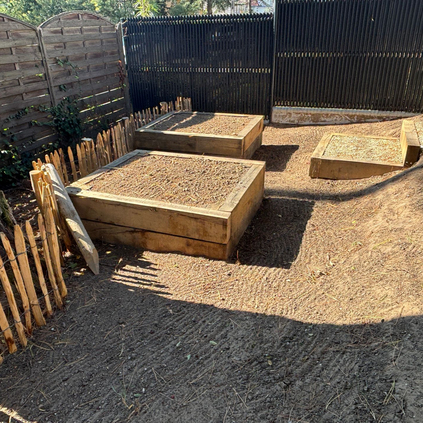 Des plates-bandes surélevées en bois remplies de terre, dans une cour recouverte de gravier et entourée de clôtures.