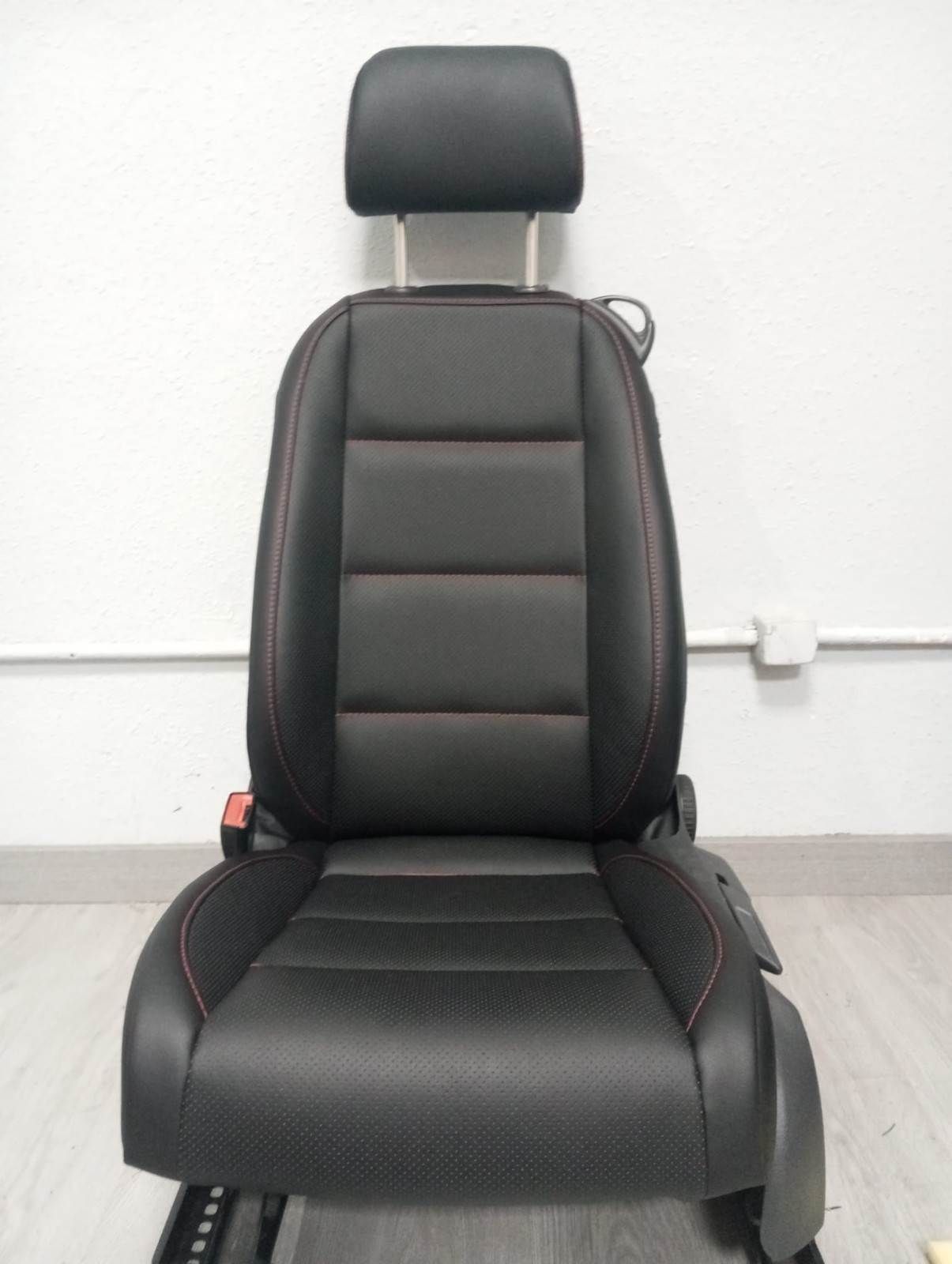 Asiento de coche negro con reposacabezas, visto de frente contra una pared blanca.