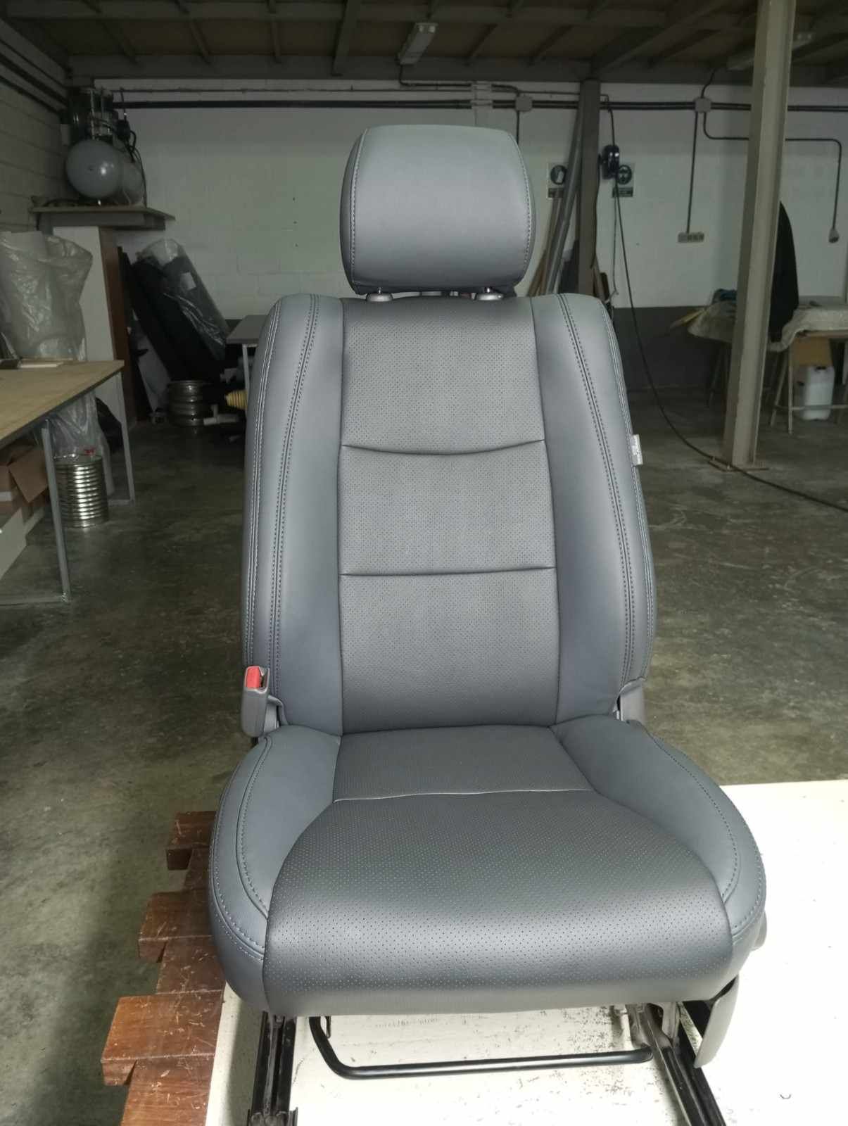 Asiento de coche gris con reposacabezas y refuerzos laterales en una zona de trabajo de un garaje.