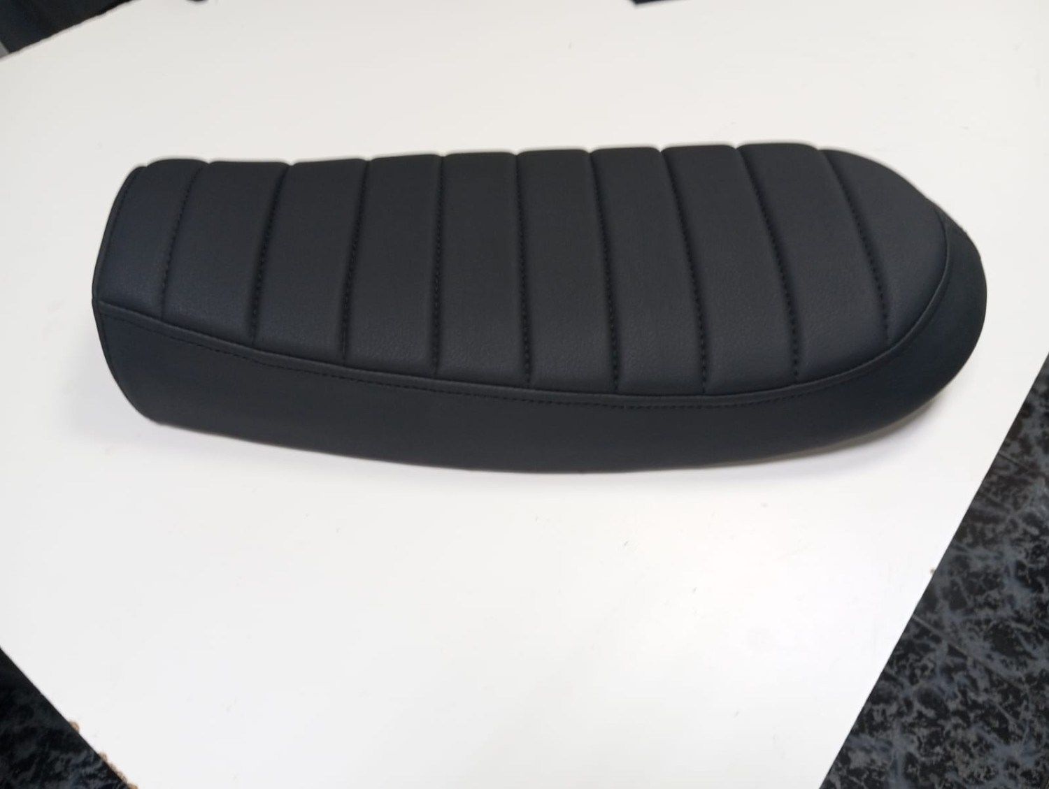 Asiento de motocicleta negro acanalado sobre una superficie blanca.