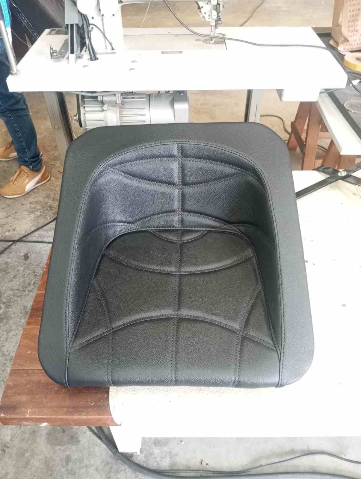 Asiento de coche negro acolchado sobre el suelo de un taller con una mesa blanca detrás.