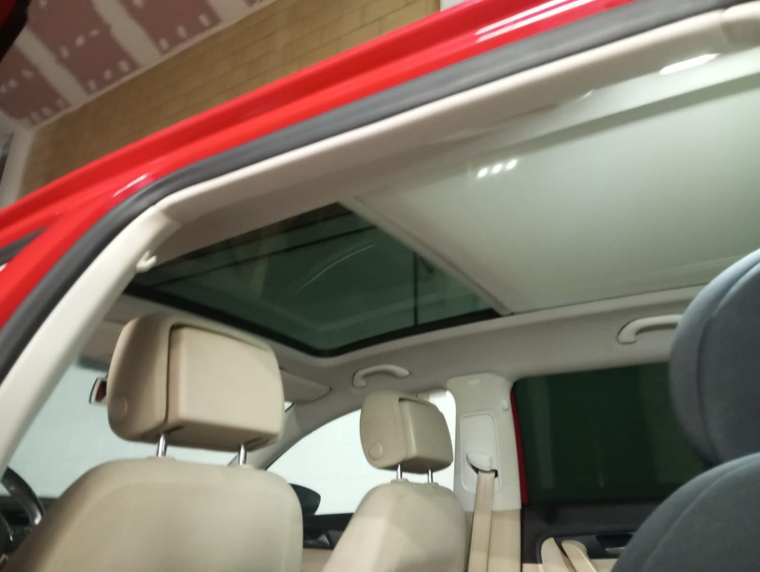 Interior del coche con asientos beige y un gran techo solar, visto a través de una puerta roja abierta.