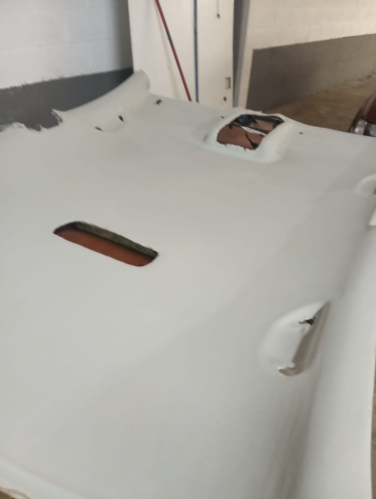 Panel de carrocería de coche pintado de blanco en un taller, con varios recortes y aberturas expuestas.