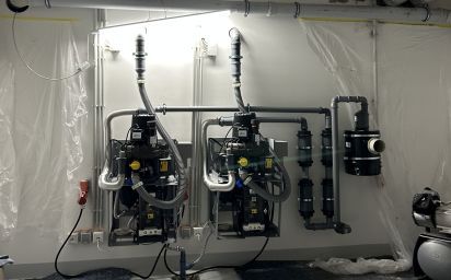 Zwei industrielle Wasserpumpen und Filter, die in einem geschlossenen Raum an einer weißen Wand montiert sind.