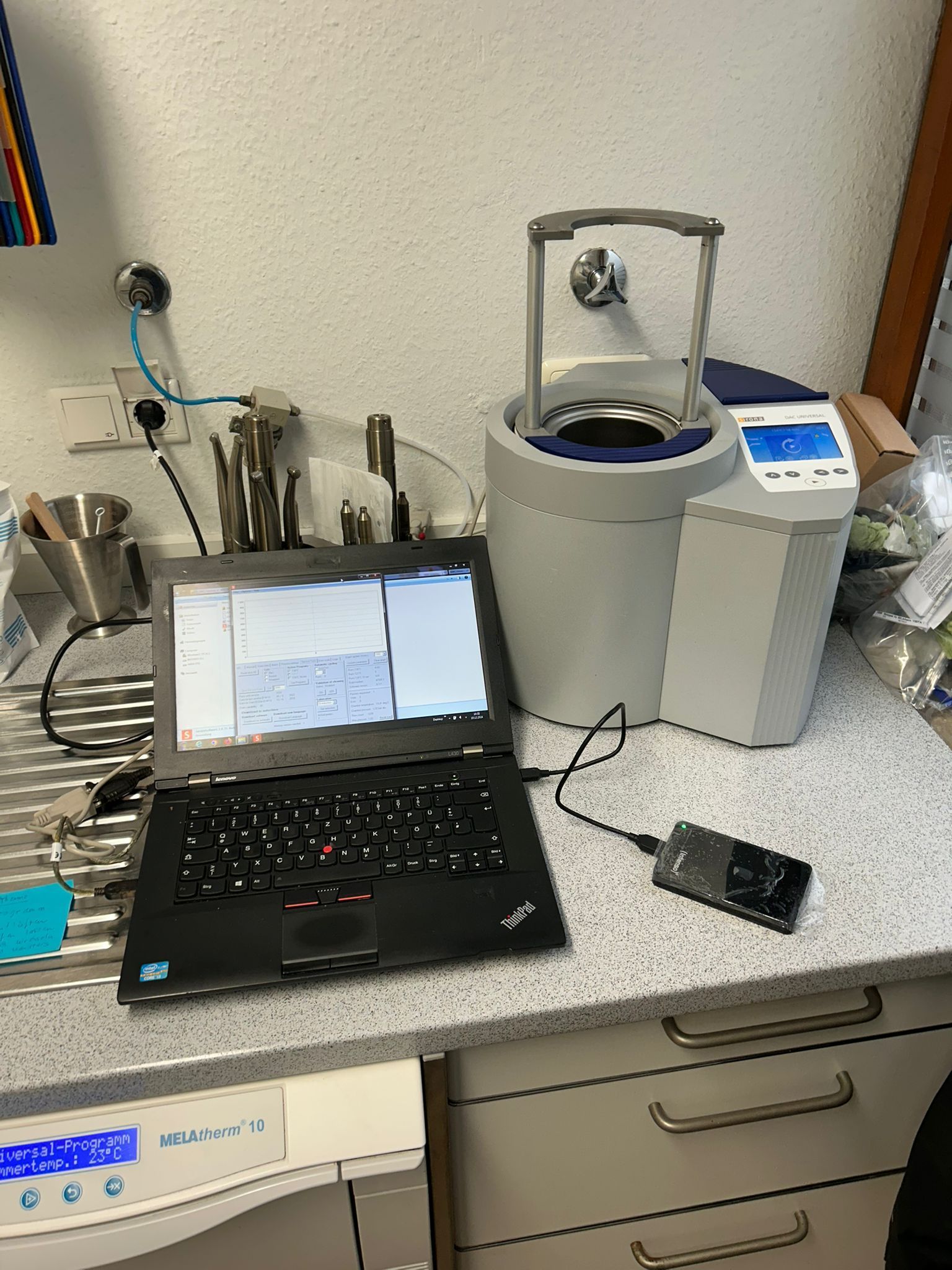 Ein Laptop, der mit Laborgeräten auf einer Arbeitsplatte verbunden ist; eine silberne Zentrifuge, möglicherweise für medizinische Analysen.