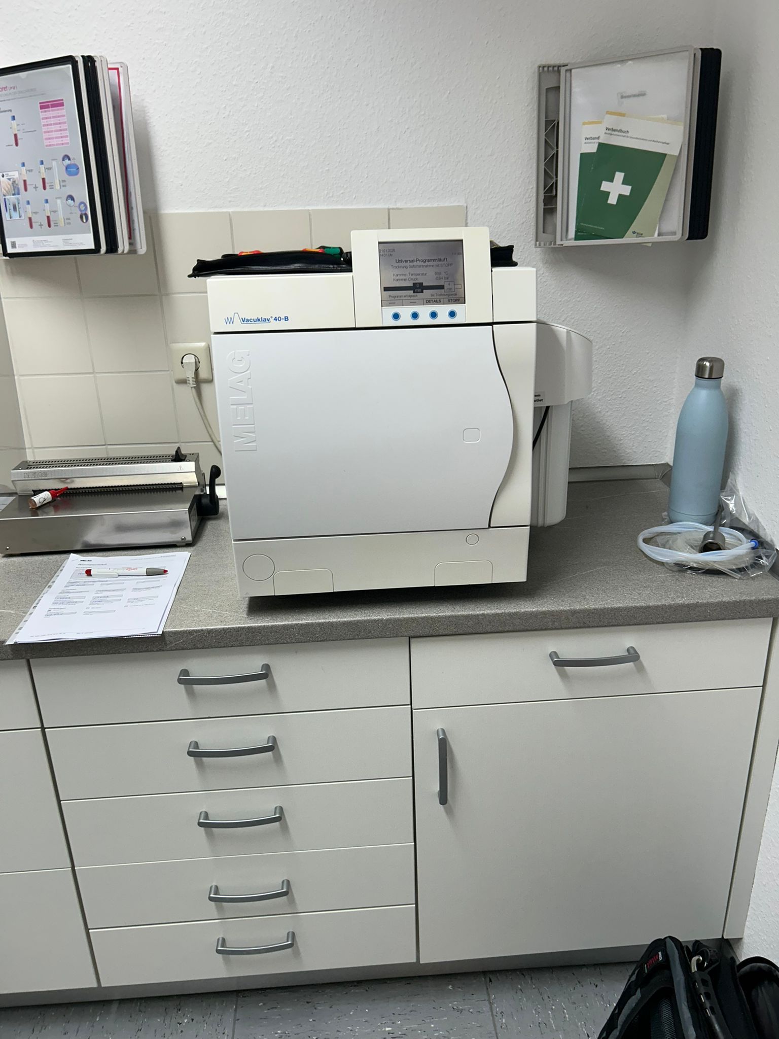 Ein weißer Dentalautoklav auf einer Arbeitsplatte mit Schränken, eine medizinische Umgebung.