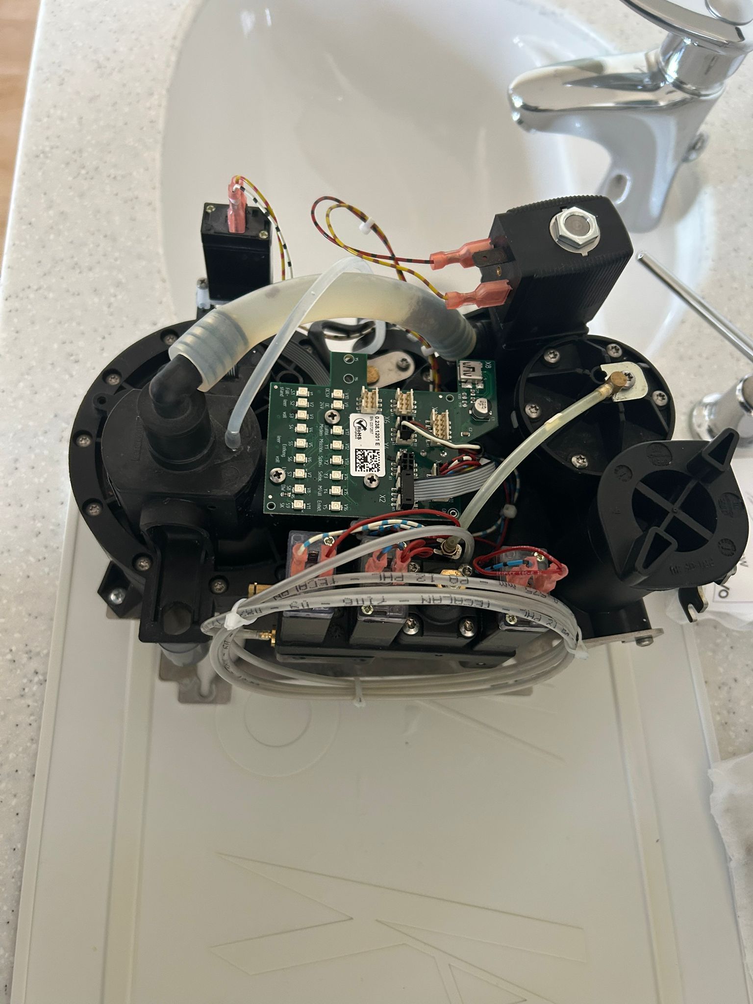 Freie Ansicht der inneren Komponenten eines schwarzen elektronischen Wasserhahns mit Leiterplatten, Schläuchen und einem weißen Waschbecken.