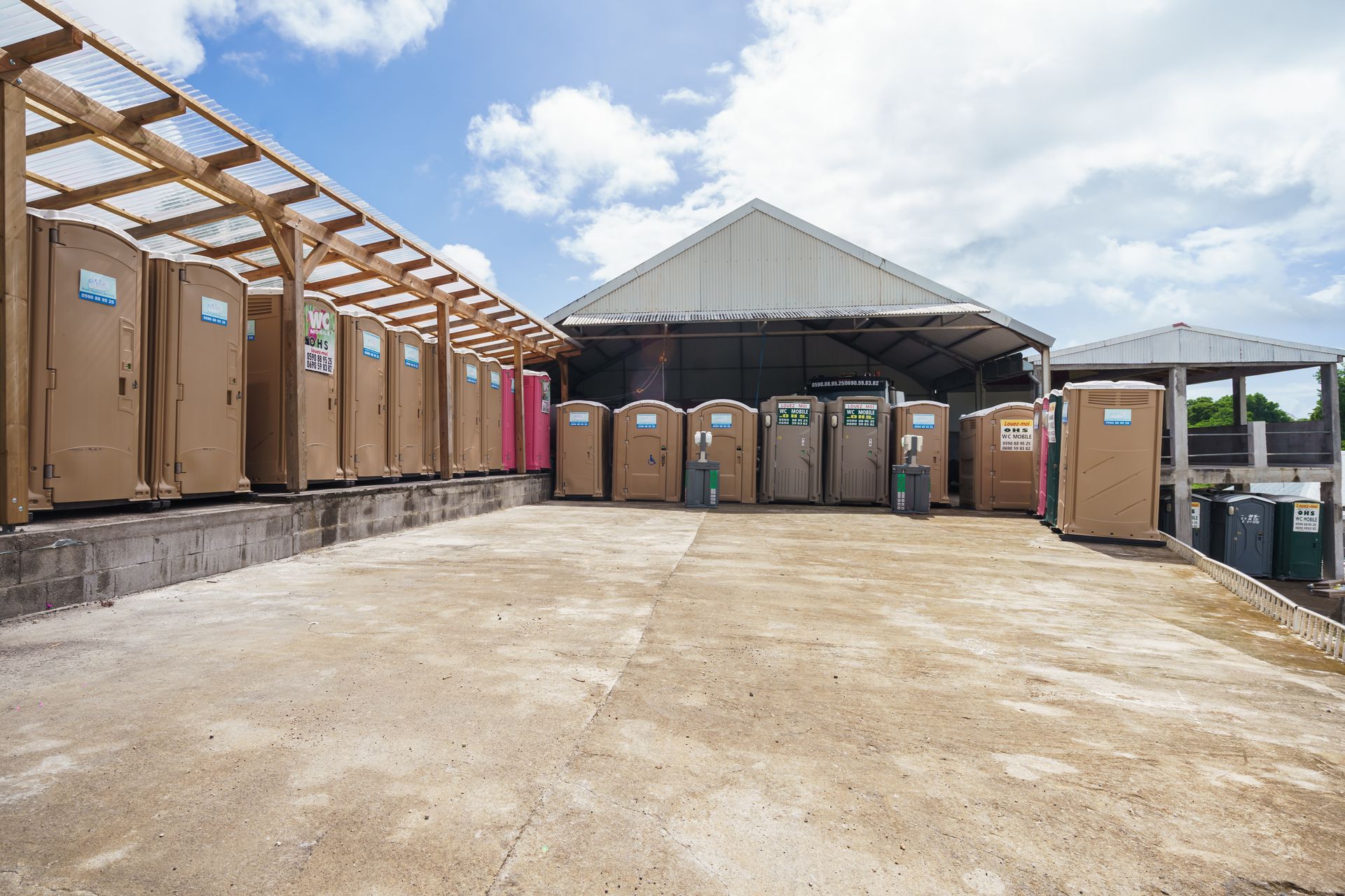 Des rangées de toilettes portables sous un abri dans une cour extérieure