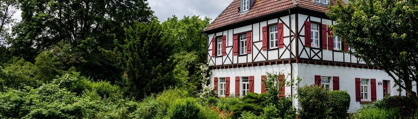 Ein weißes Haus mit roten Fensterläden ist von Bäumen umgeben.