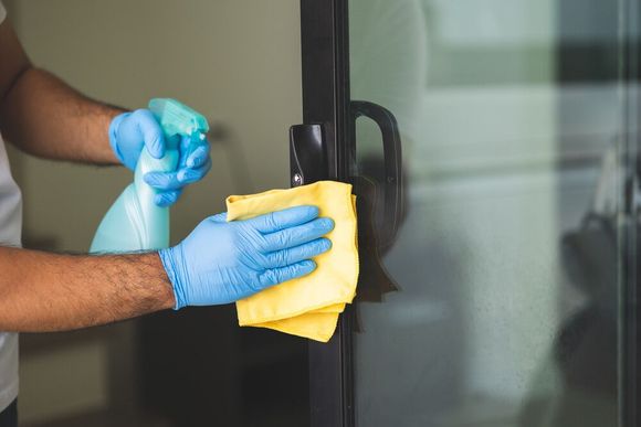 Un hombre que lleva guantes azules está limpiando una puerta de vidrio con un paño.
