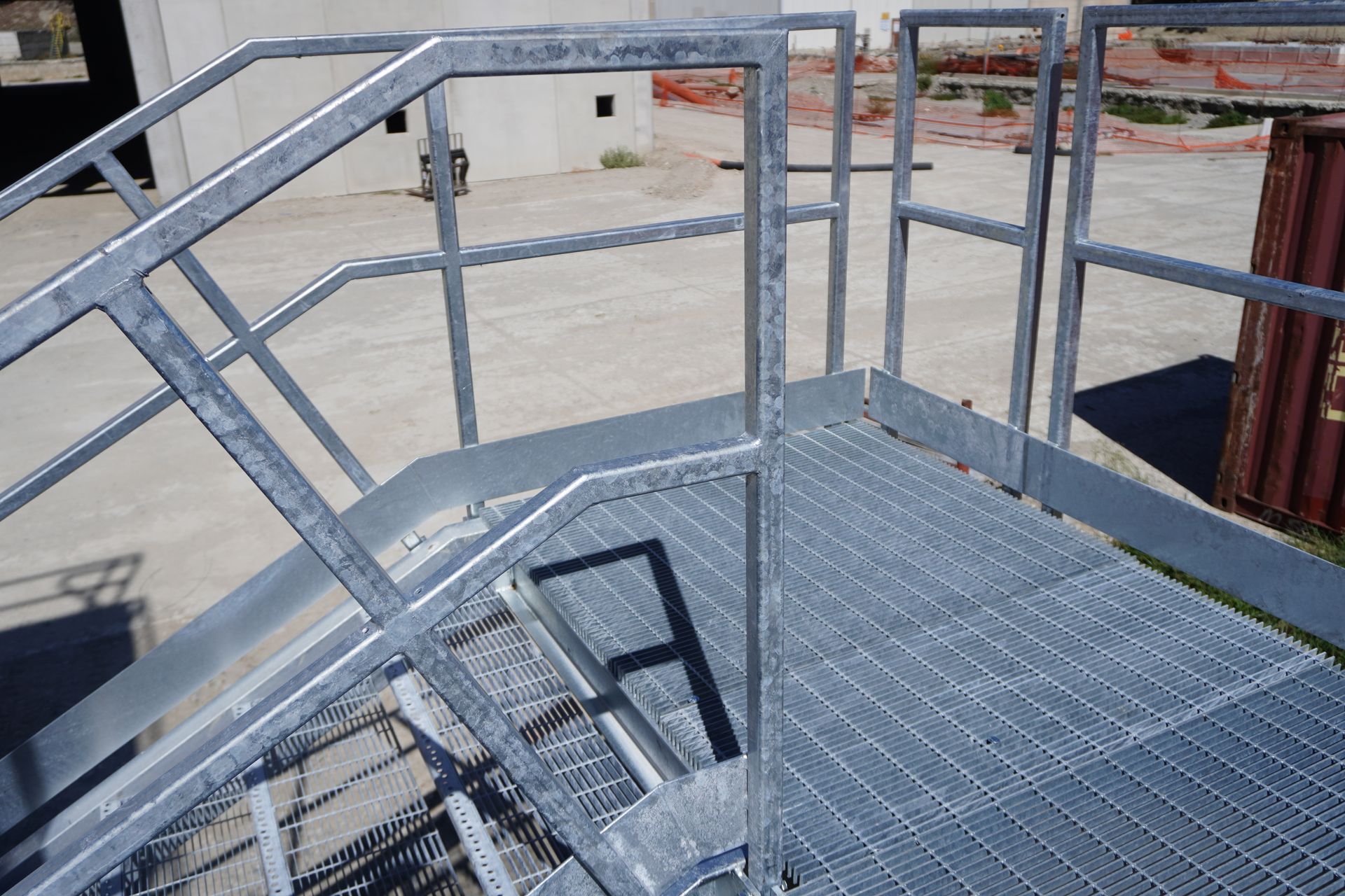 Vue en plongée d'un escalier industriel en acier galvanisé et d'une plateforme d'accès avec des garde-corps métalliques.