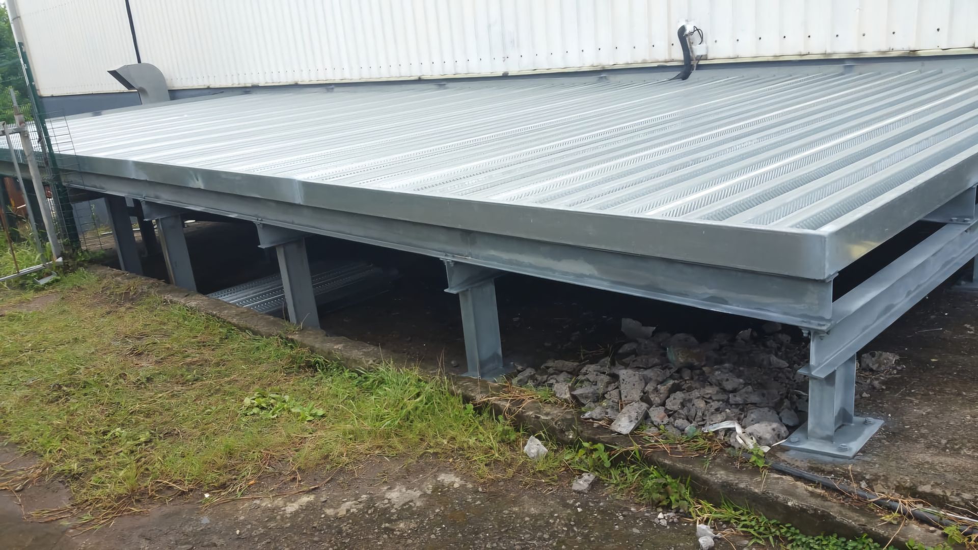 Plateforme métallique rectangulaire à surface ondulée, soutenue par une structure de poteaux en acier gris.