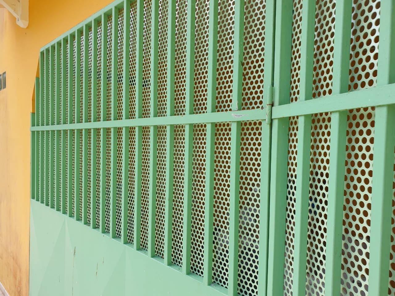 Une grille de sécurité en métal vert clair, à barreaux verticaux et à panneaux perforés.