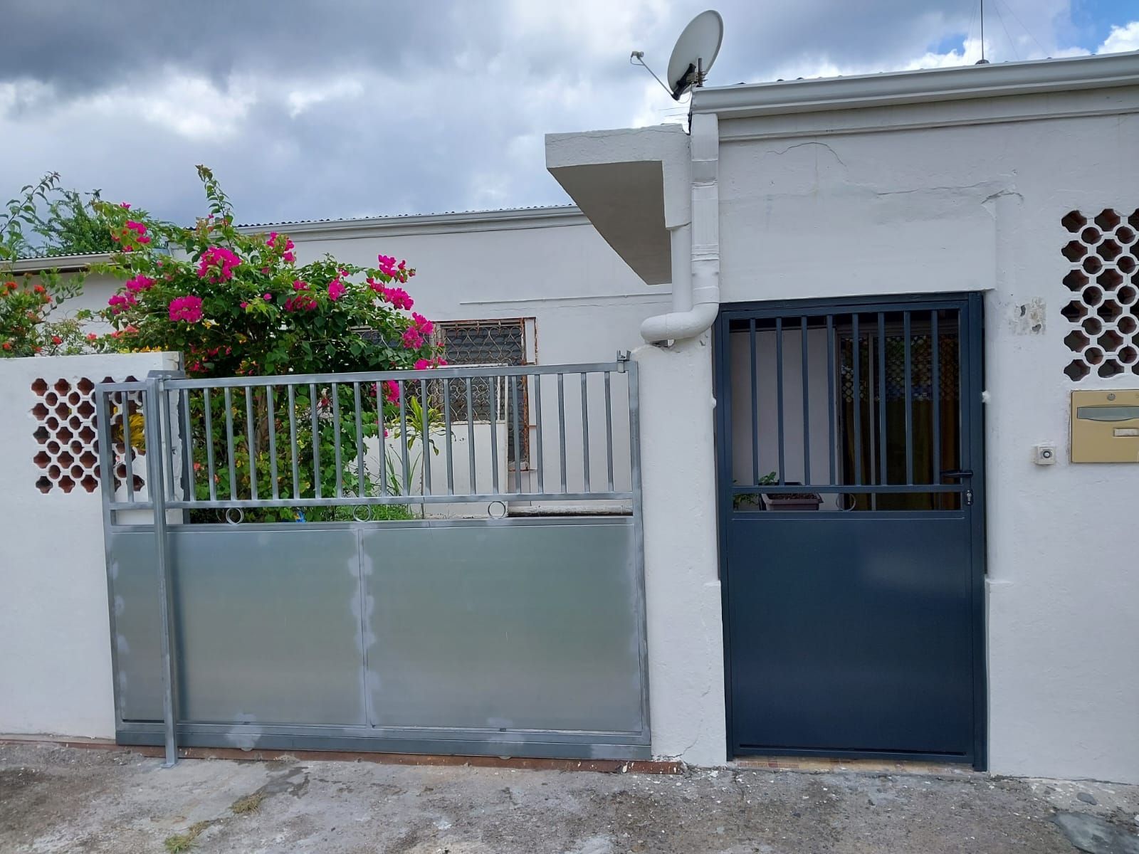 L'entrée d'un bâtiment blanc, avec un portail coulissant en fer et une porte en métal.