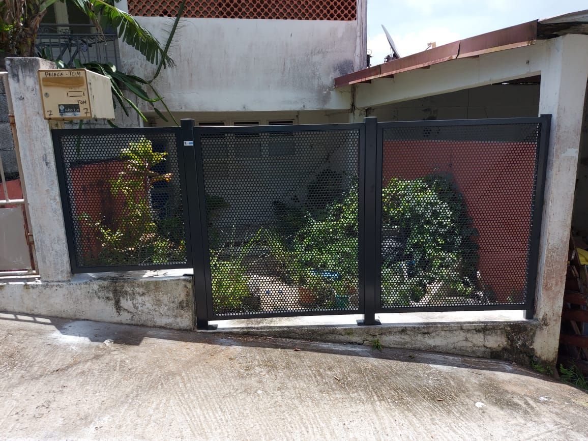 Une clôture en métal noir avec des panneaux en treillis à motif losange est installée devant une maison.