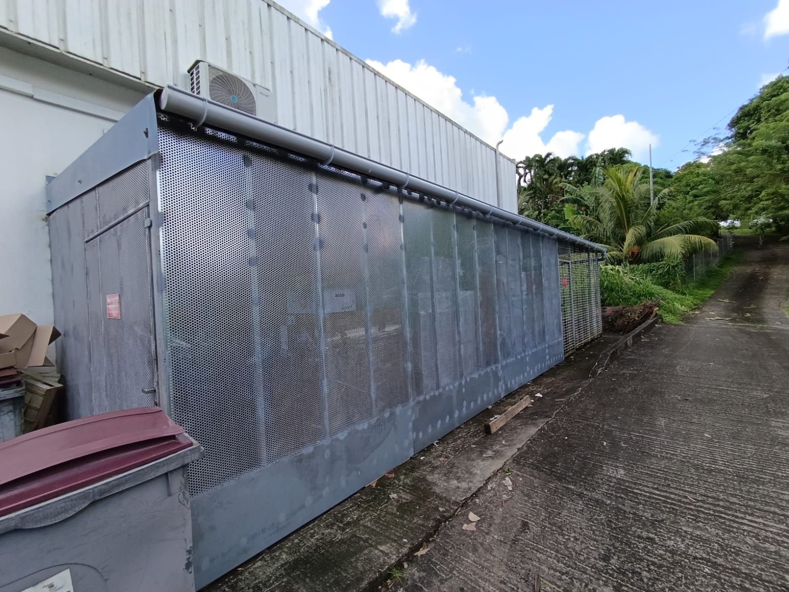 Une longue structure métallique grise aux panneaux perforés est adossée à la façade d'un bâtiment.