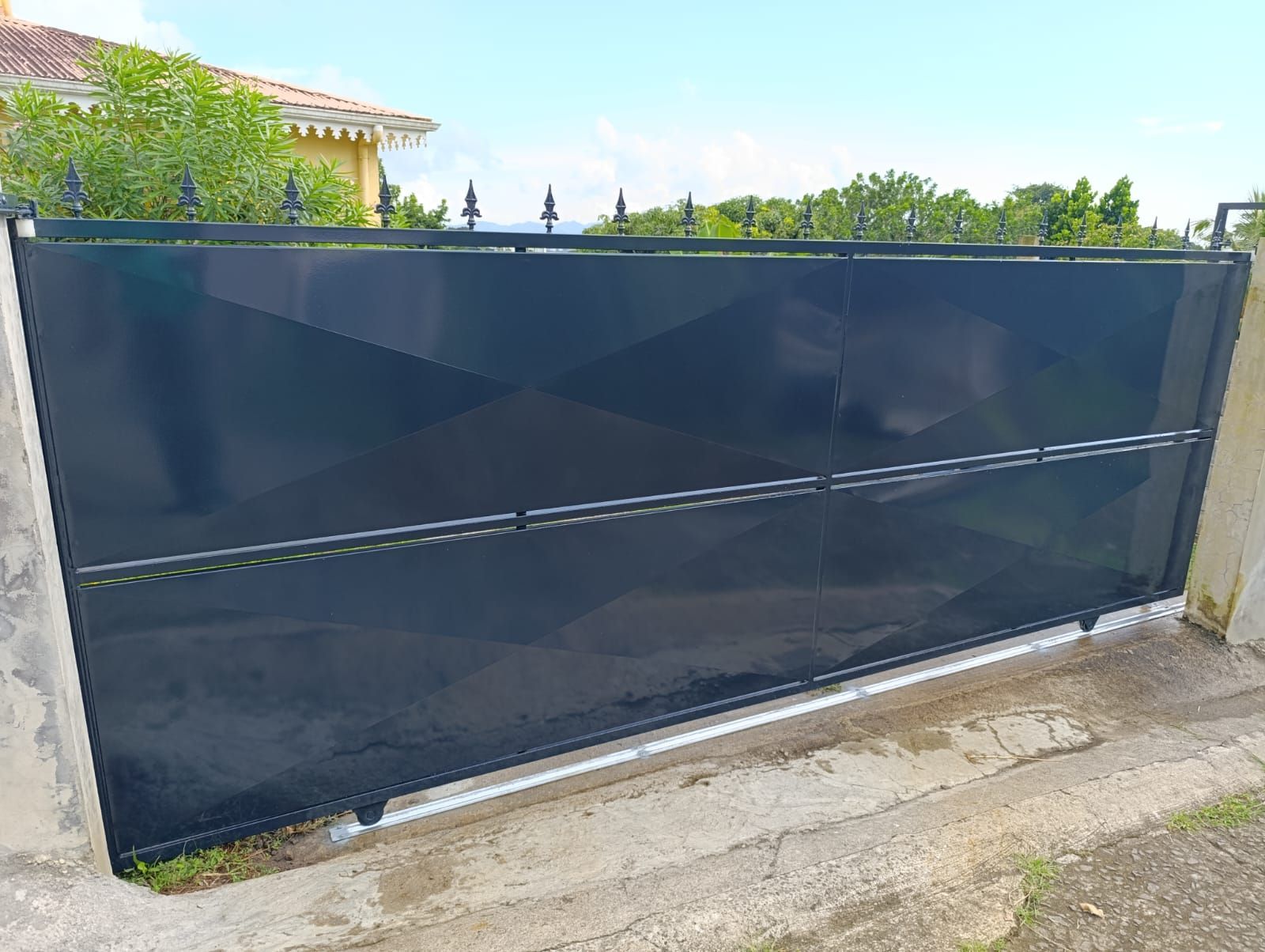 Un portail coulissant horizontal noir massif, muni de pointes métalliques sur le dessus.