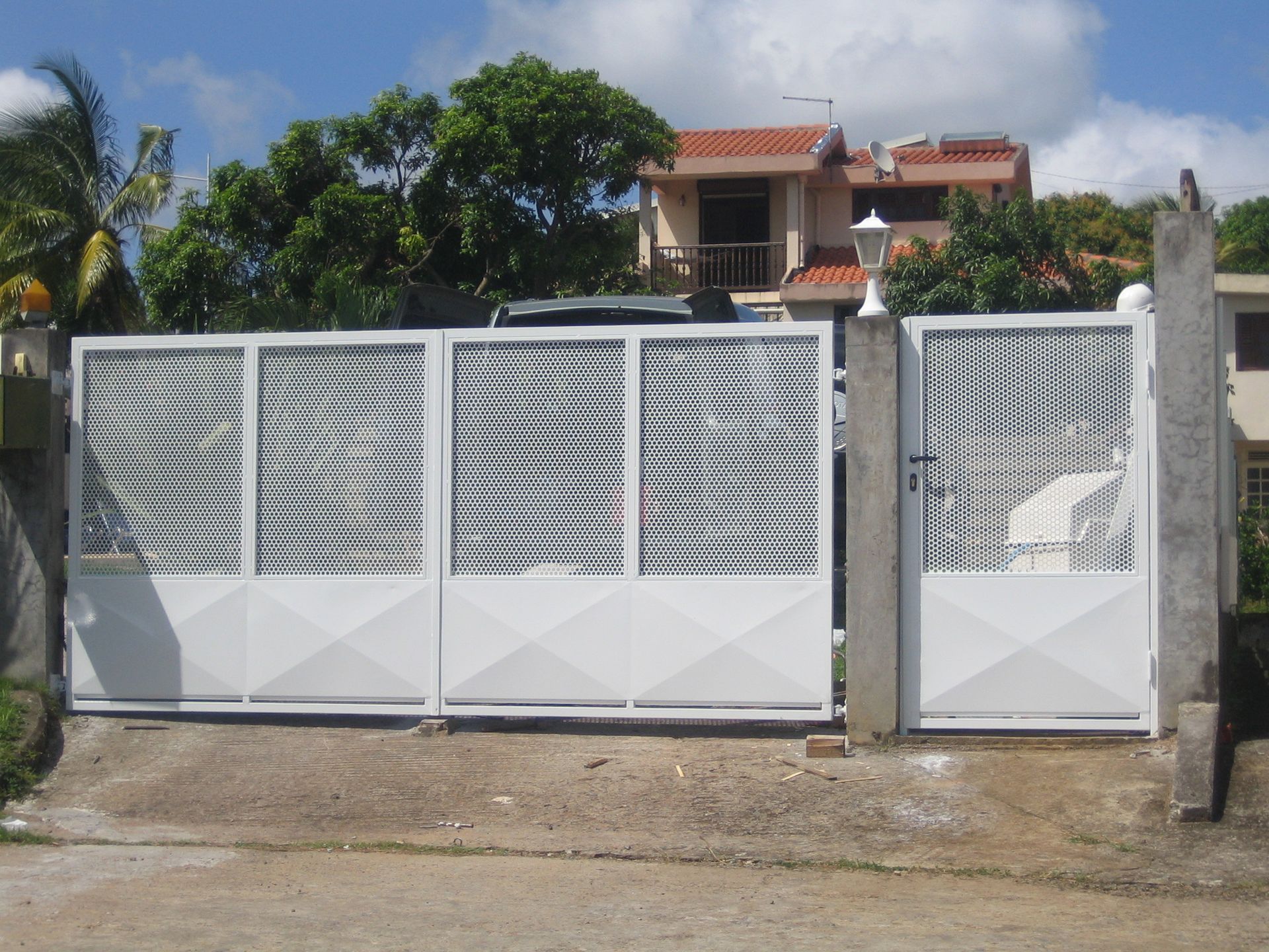 Un portail d'allée en métal blanc avec des panneaux supérieurs en maille ondulée et un portillon piéton assorti.