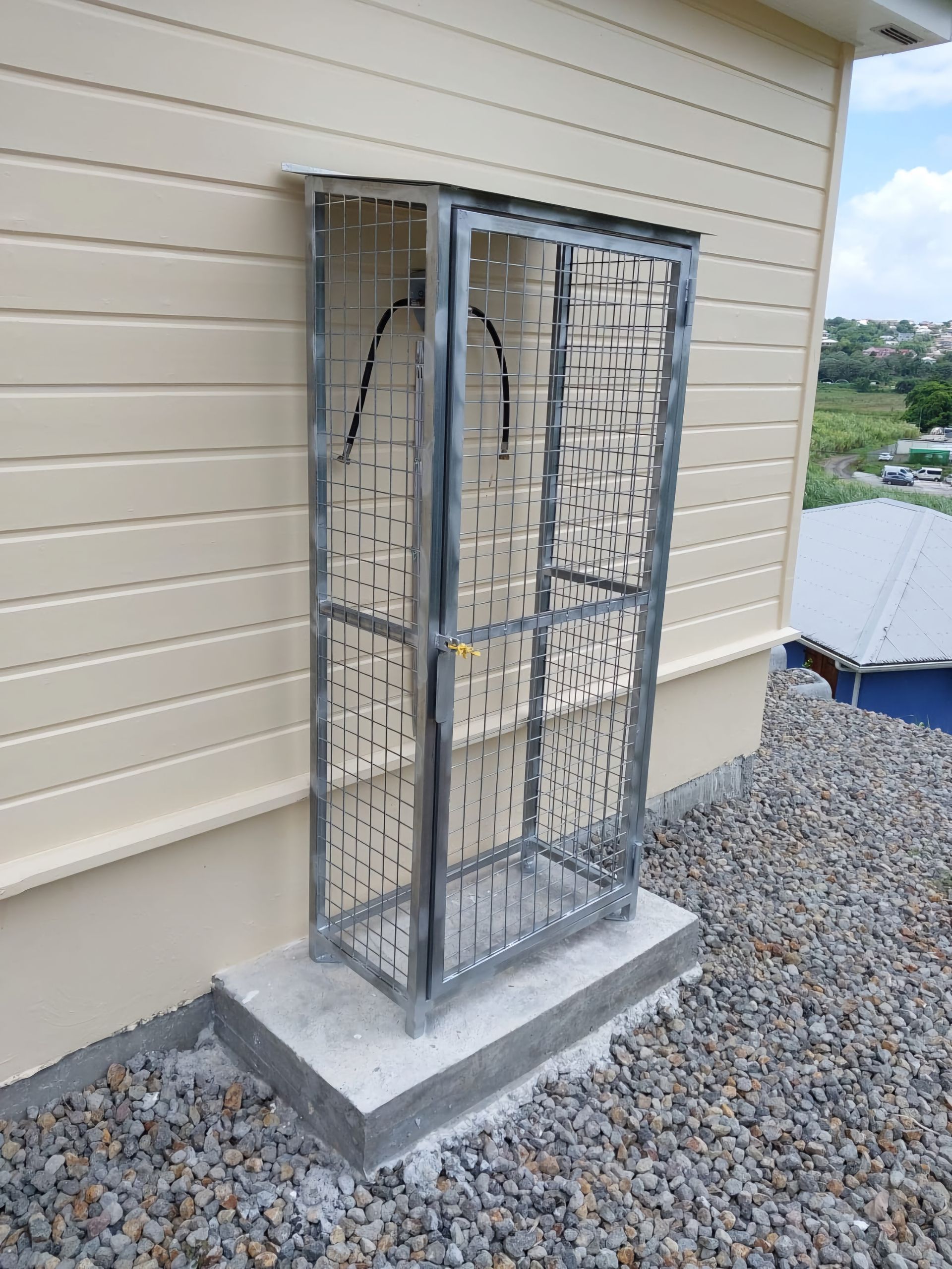 Une grande armoire métallique grillagée repose sur un socle en béton.