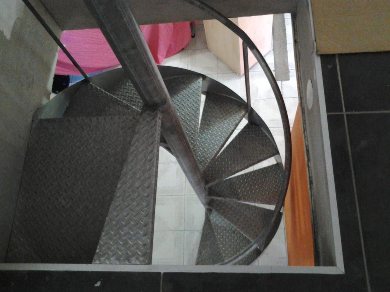 Vue plongeante d'un étroit escalier industriel en colimaçon métallique.