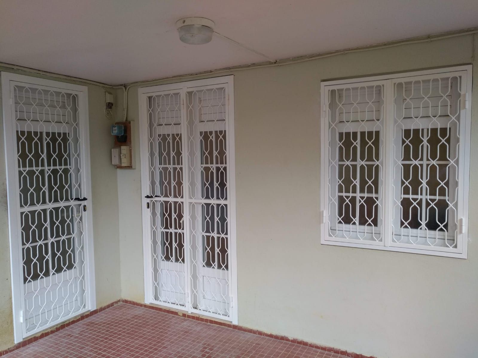 Un mur clair orné d'une porte et d'une fenêtre blanches avec des grilles de protection en métal blanches.