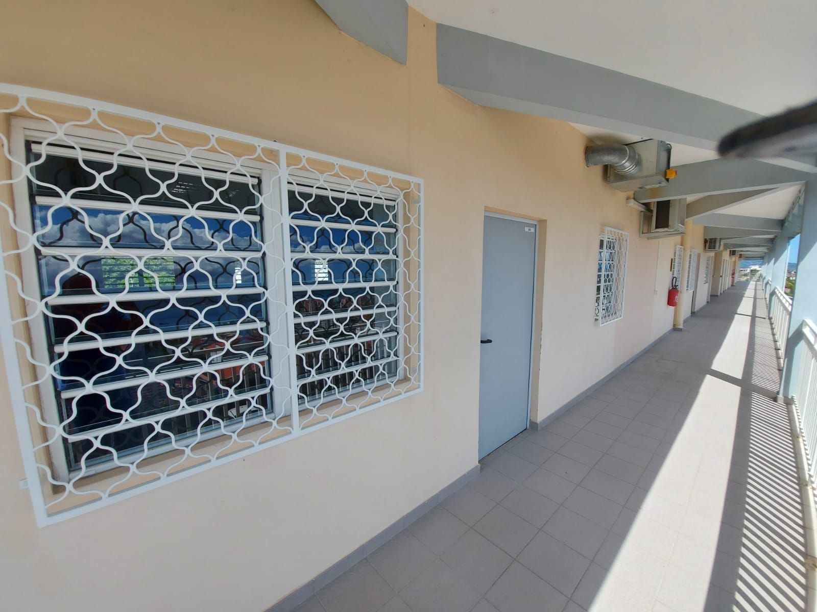 Une fenêtre à grille de sécurité et une porte grise, donnant sur un balcon ouvert.