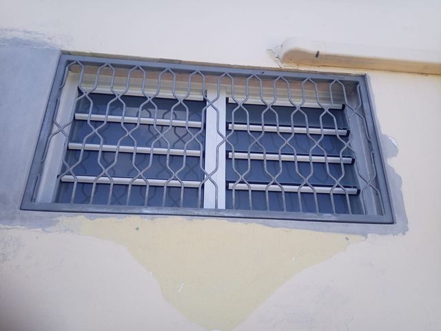 Une fenêtre rectangulaire avec une grille de sécurité en métal gris.