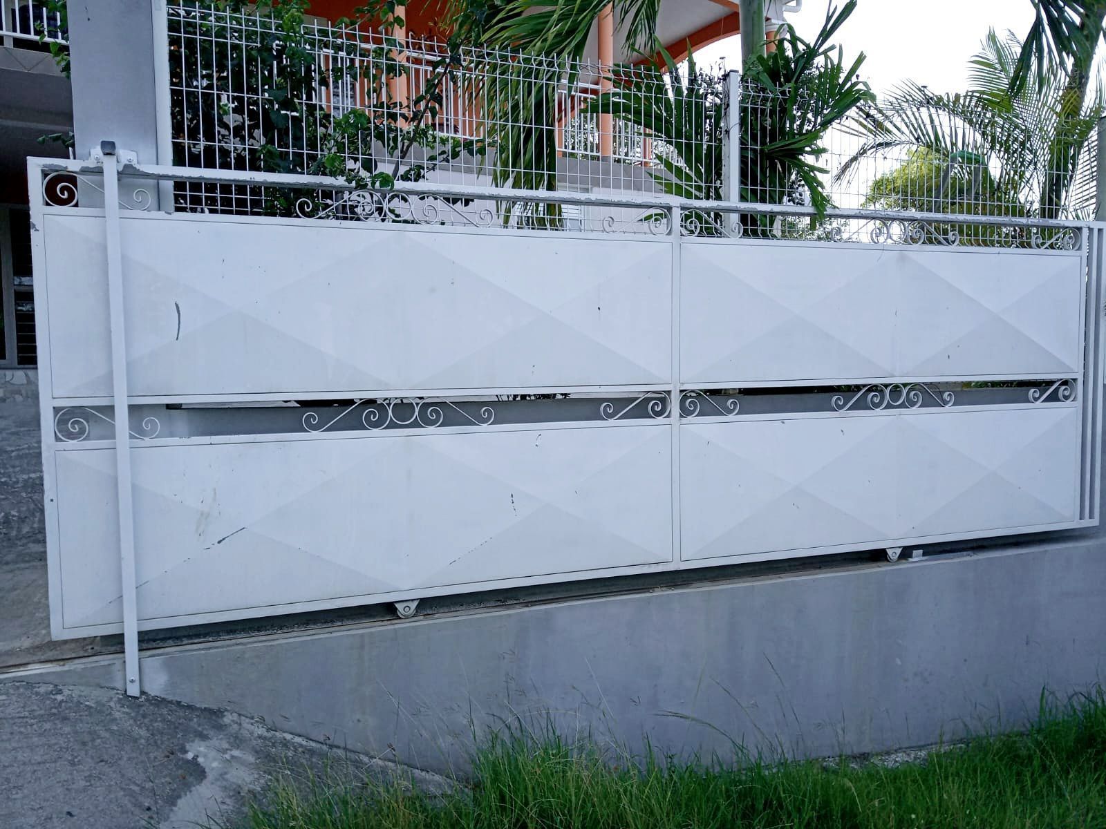 Un portail rectangulaire en métal blanc orné d'un motif géométrique en losanges et d'un panneau central horizontal décoratif.