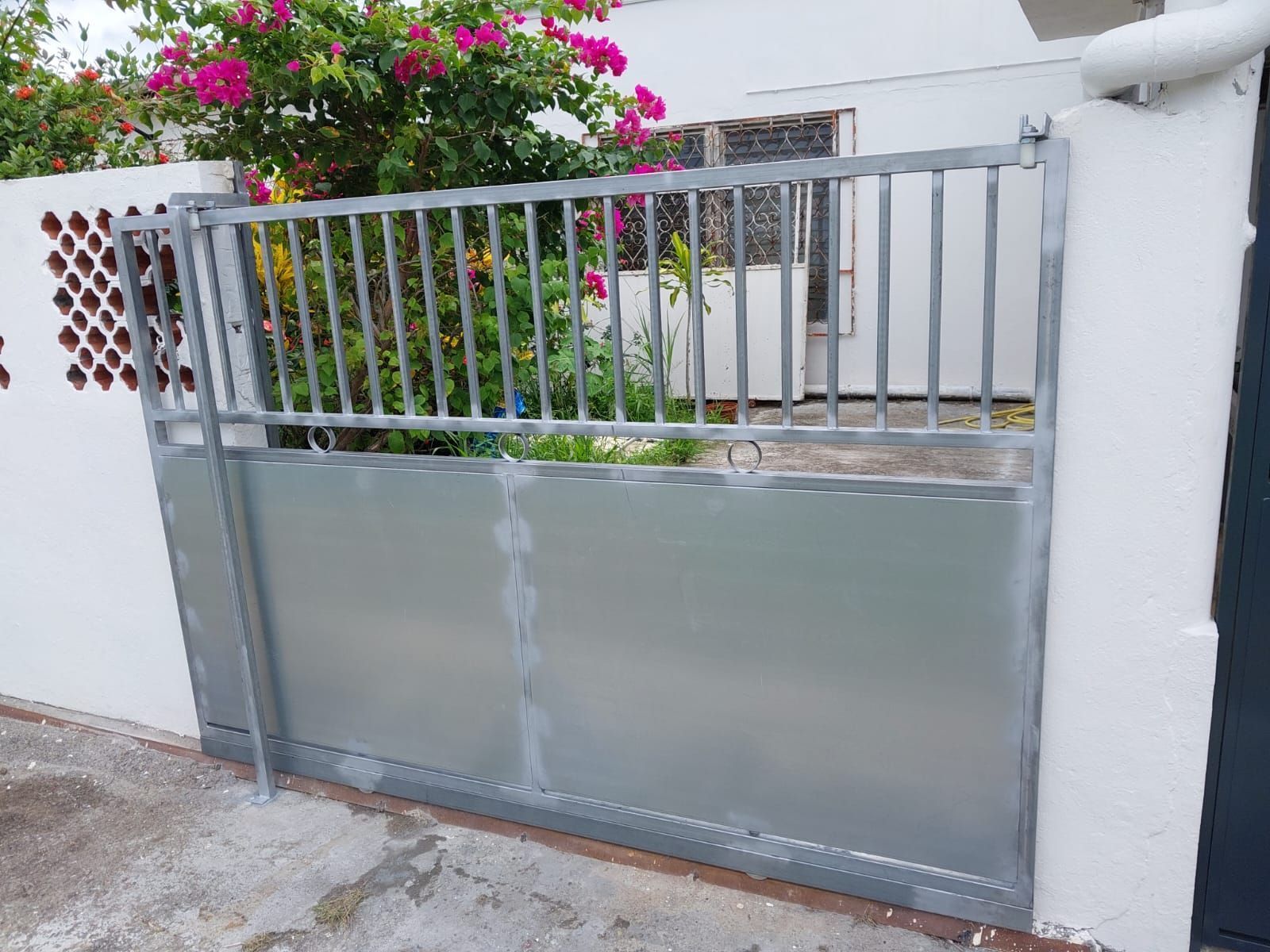 Un portail coulissant en métal avec des barreaux verticaux en haut et un panneau plein en bas.