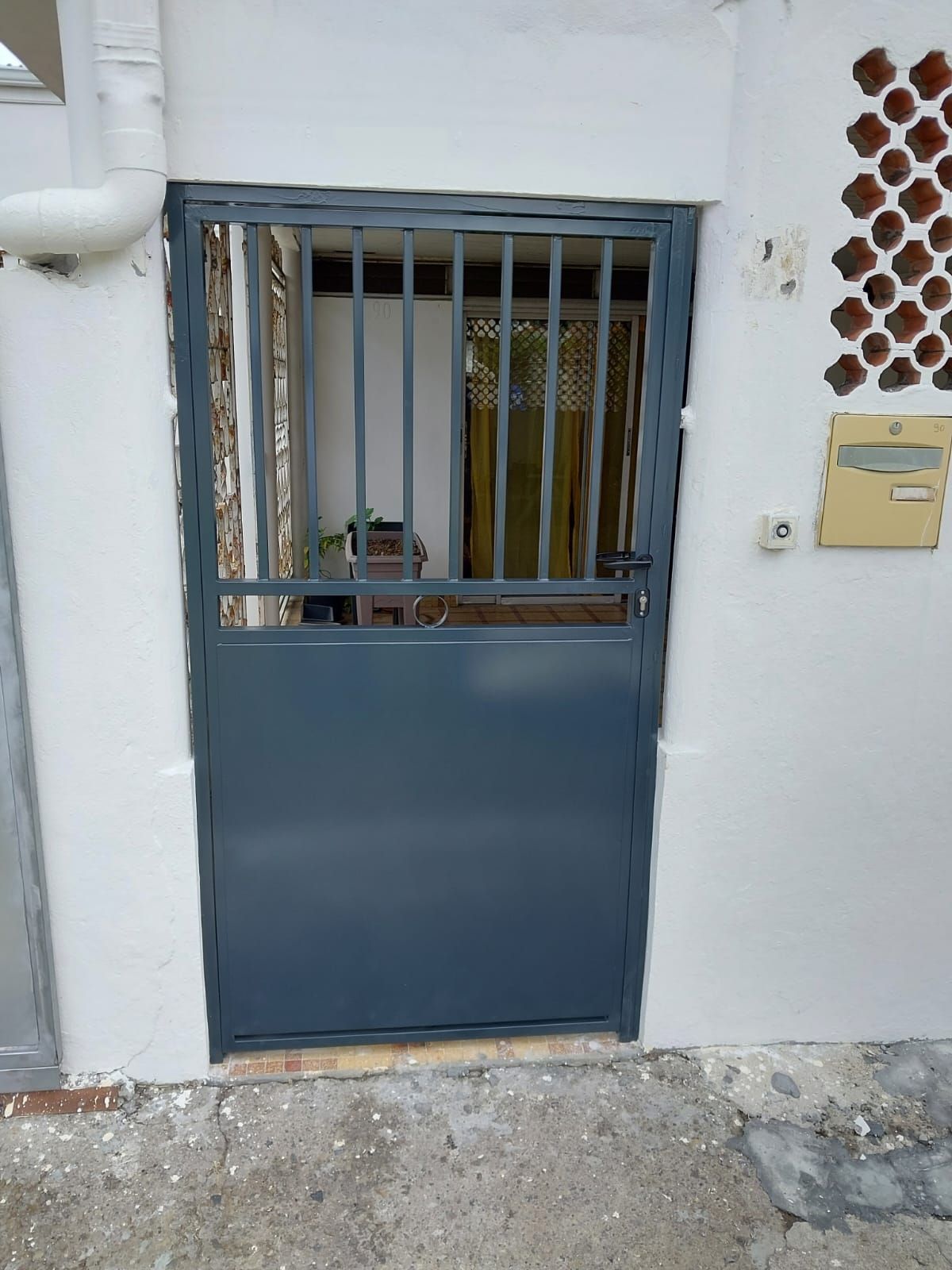 Une porte en métal gris foncé avec une partie supérieure à barreaux verticaux.