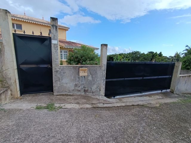 Un portillon piéton en métal noir et un portail coulissant assorti plus large, encastrés dans un mur en béton.