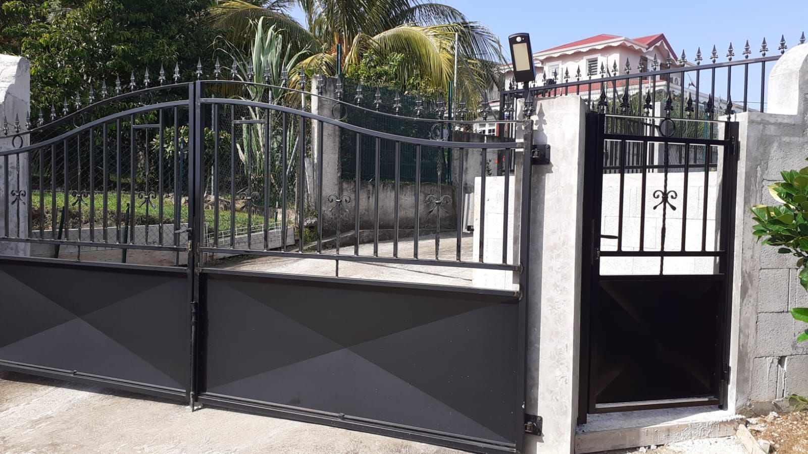 Un grand portail d'allée en métal noir jouxte un portillon piéton plus petit.