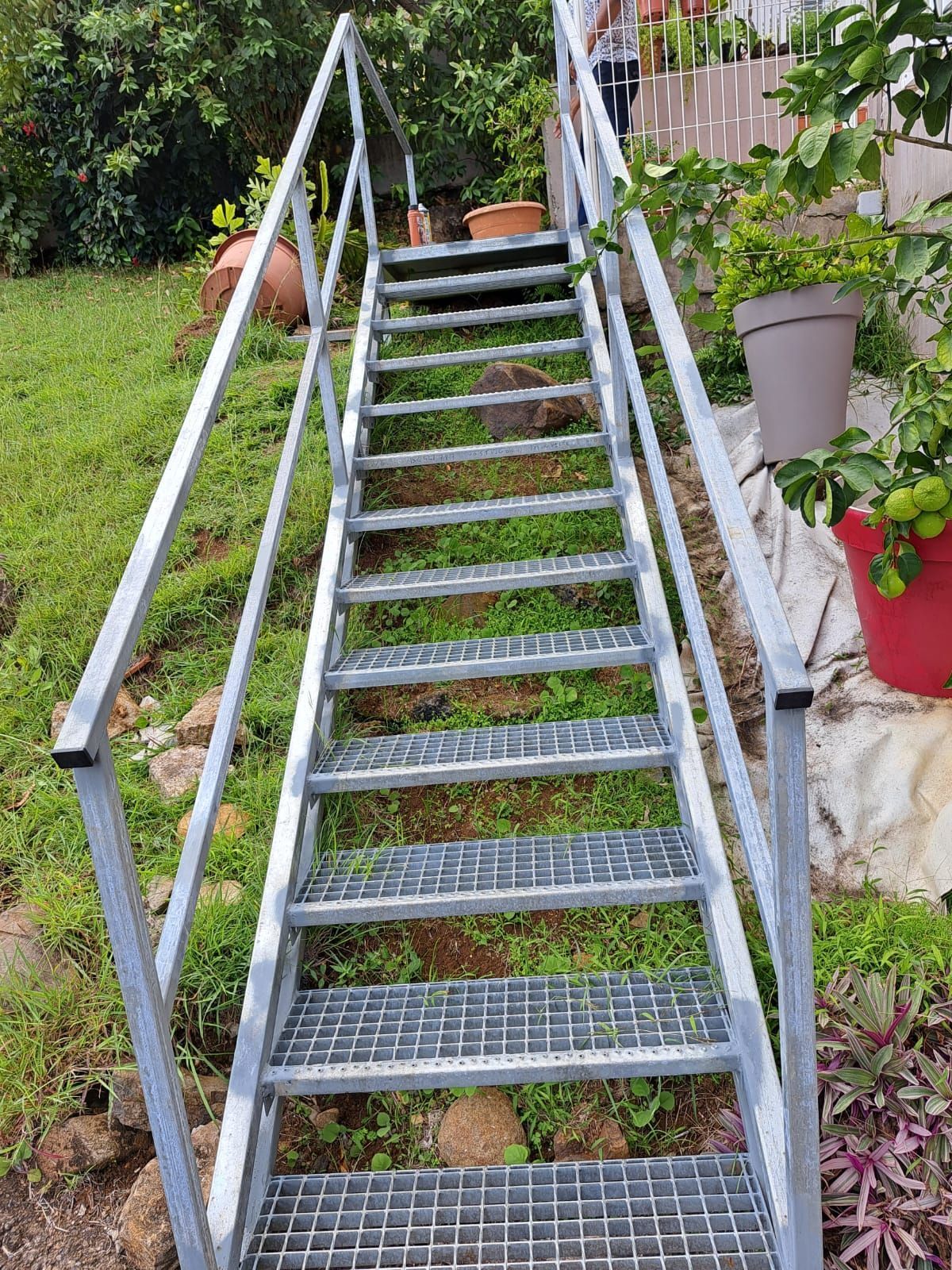 Un escalier raide en métal argenté, muni d'une rampe.