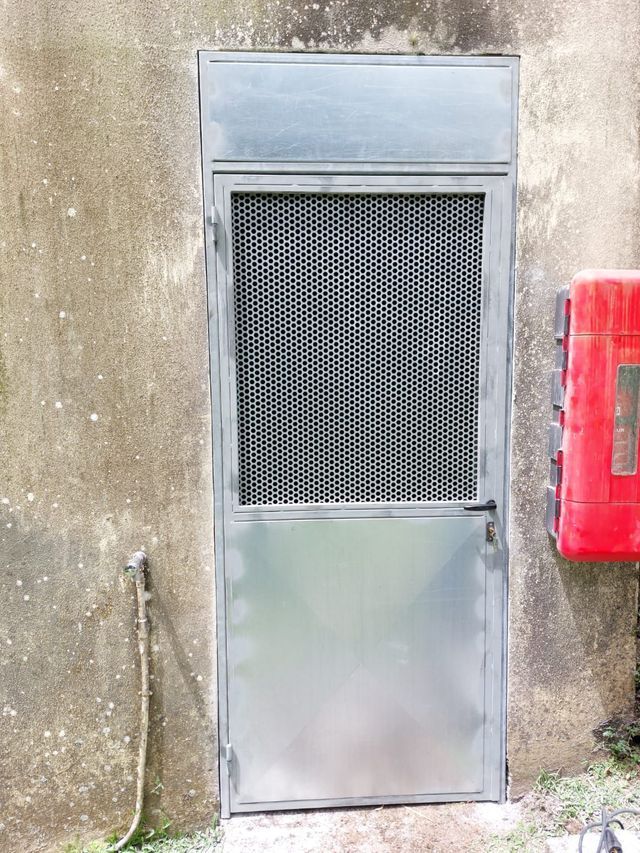 Une porte en métal gris avec un panneau supérieur en maille à motif losange.