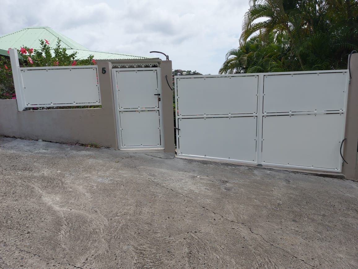 Un portillon piéton en métal blanc et un portail pour allée carrossable sont encastrés dans un muret beige.